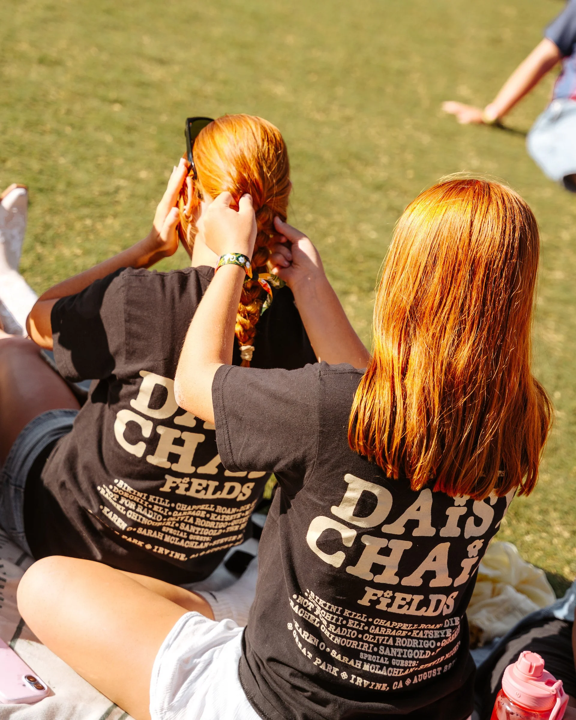 "Two festivalgoers in matching Daisy Chain Fields t-shirts sit on the grass at the Great Park in Irvine, California."