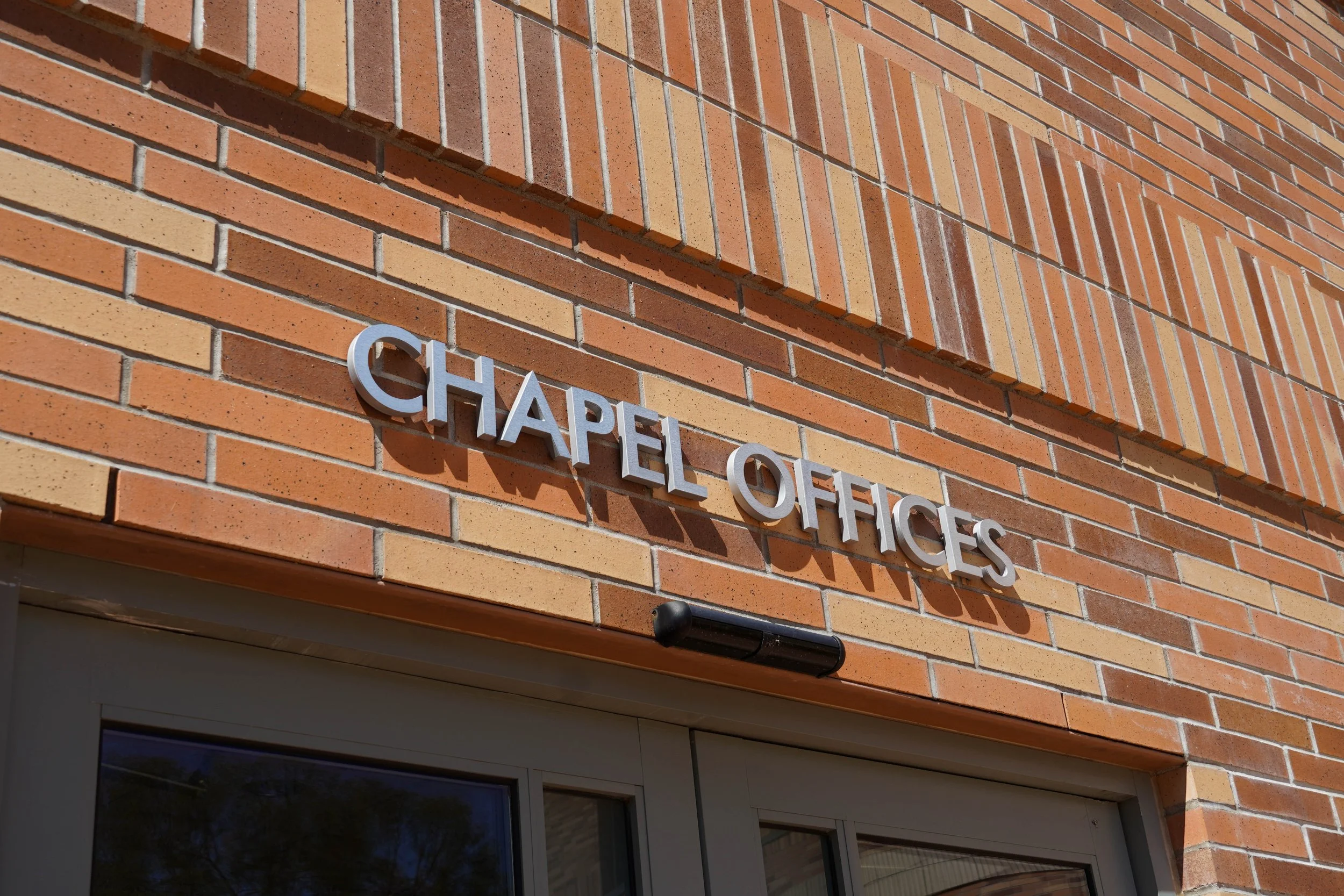 Orange brick wall above a doorway with a sign saying "Chapel Offices" writen in silver text.