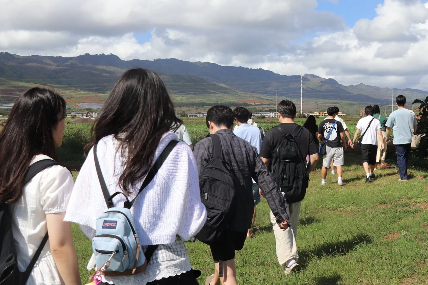 Students with backpacks walk across grass.