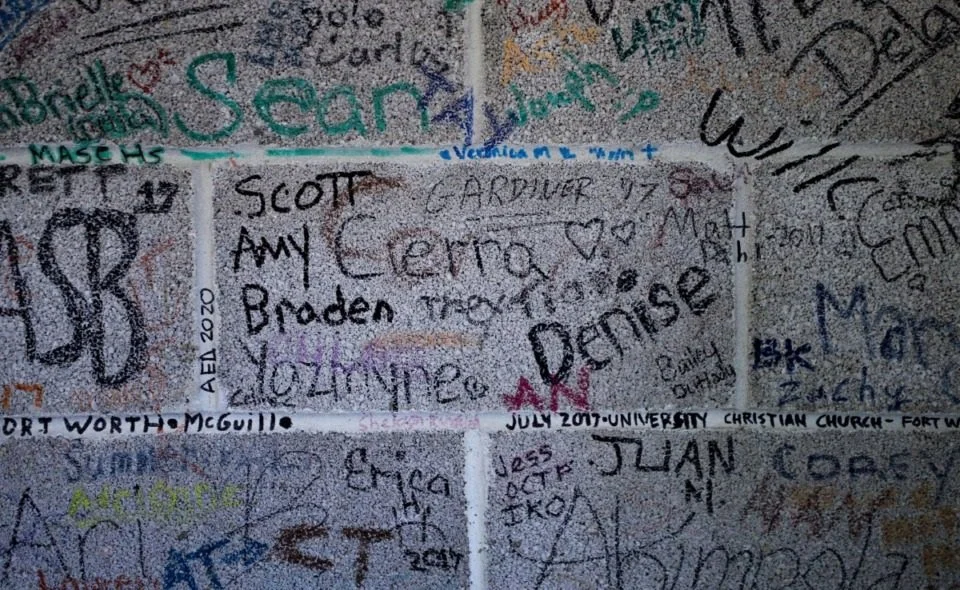 Wall decorated with numerous handwritten signatures, names, and messages in various colors and styles.