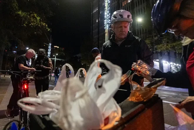 People wearing helmets gather around a table with plastic swan-shaped objects on a city street at night.