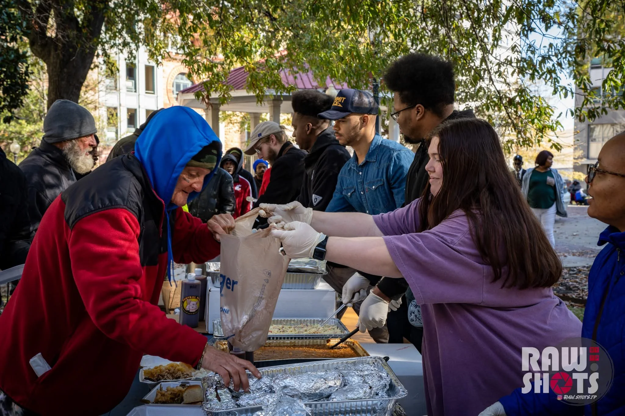 People serving food at an outdoor event under a large tree