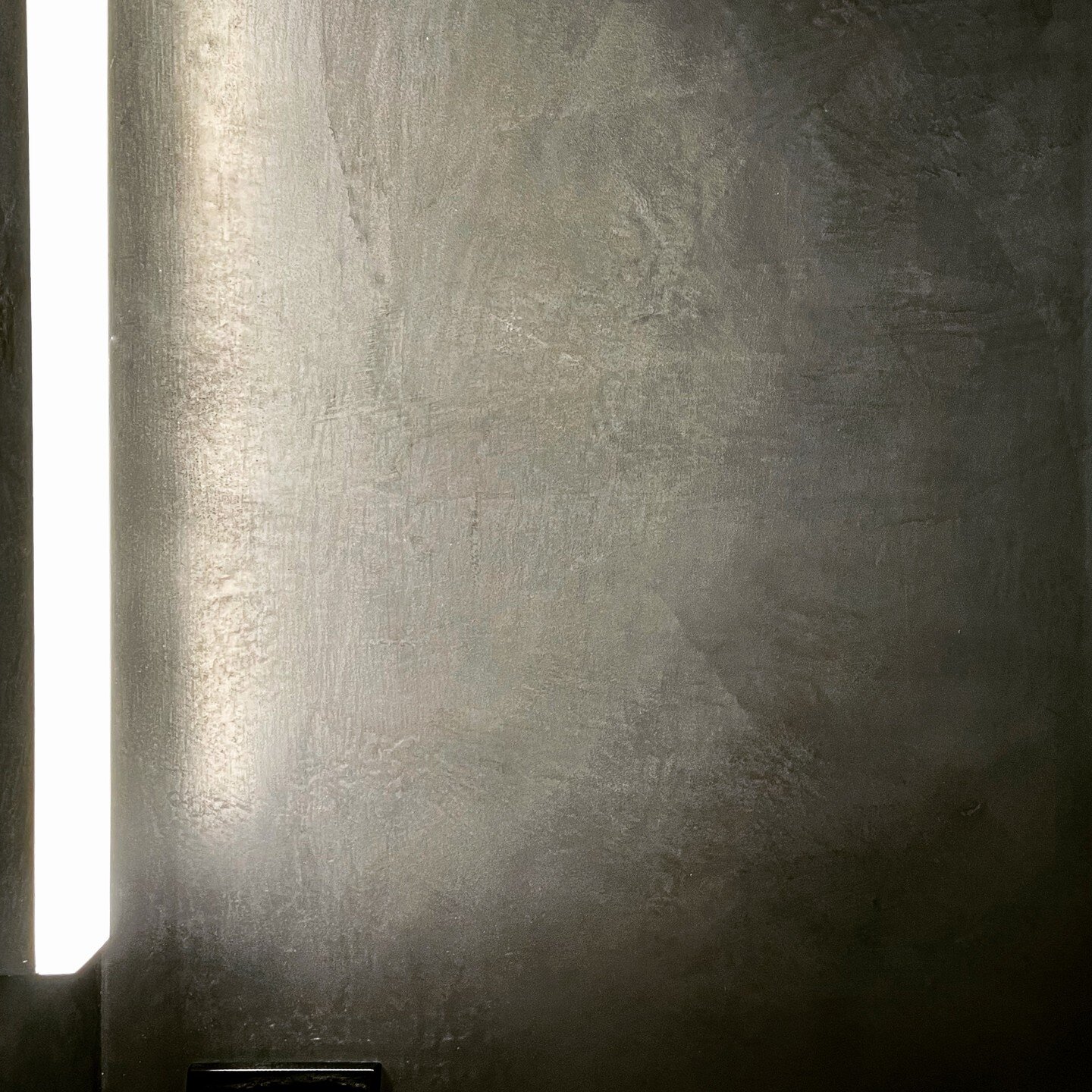 Very dark plaster, very bright light. This bathroom feels like it was carved out of anthracite. Ceiling, walls, and floor in black with a burnish.