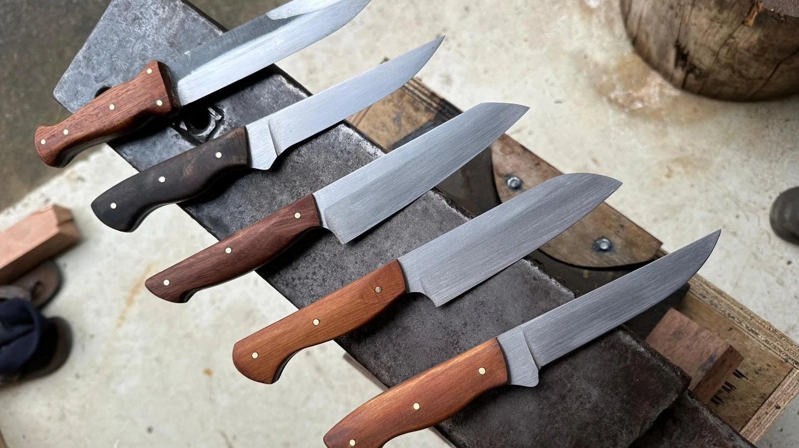 Five knives displayed on an anvil a mixture of styles and wooden handles