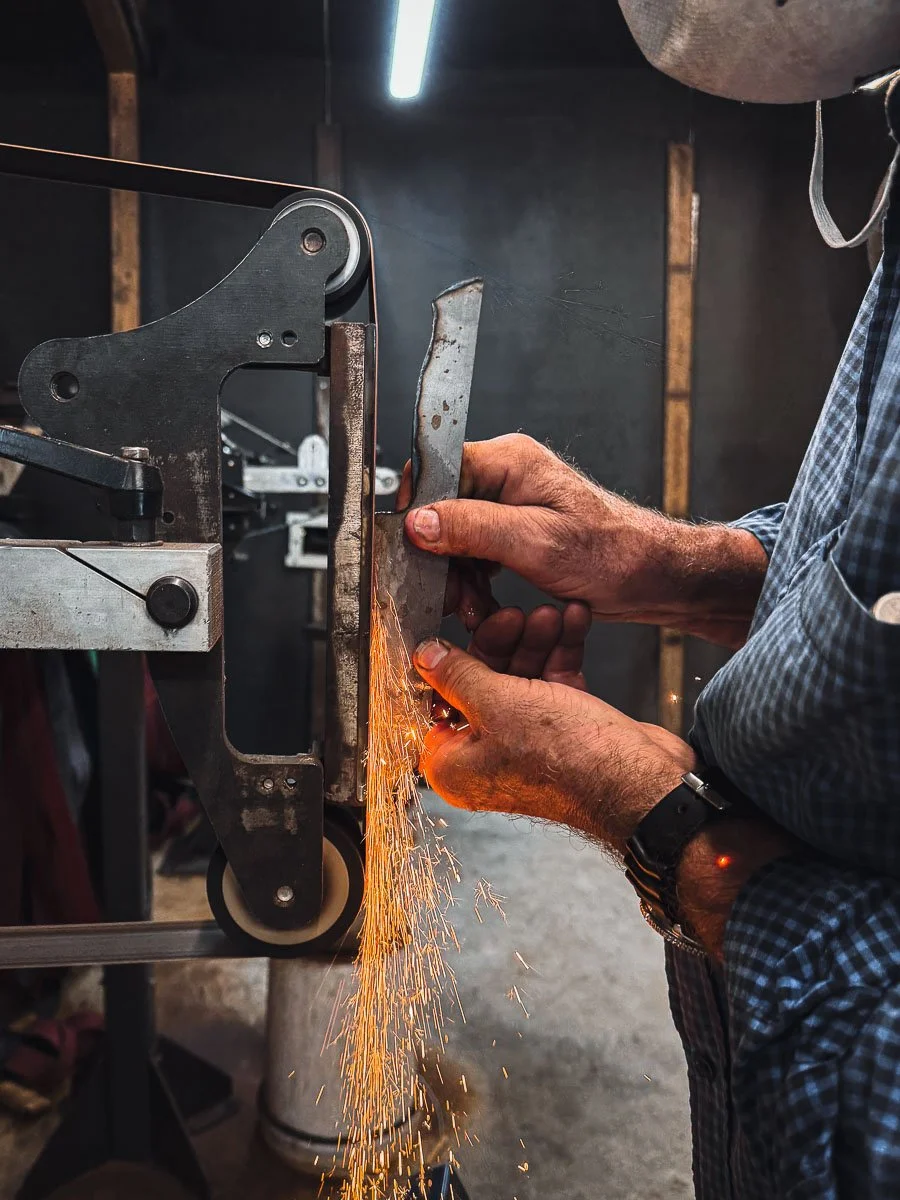 knifemaker grinding santoku chefs knife on belt grinder, orange sparks visible