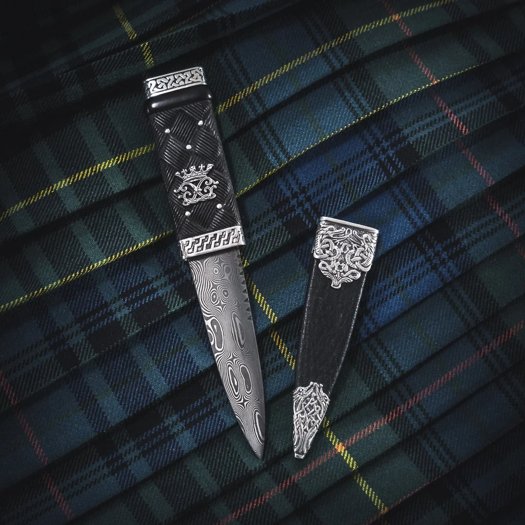 An ornate traditional hand made scottish Sgian Dubh knife with intricate designs and patterns, resting on tartan fabric.