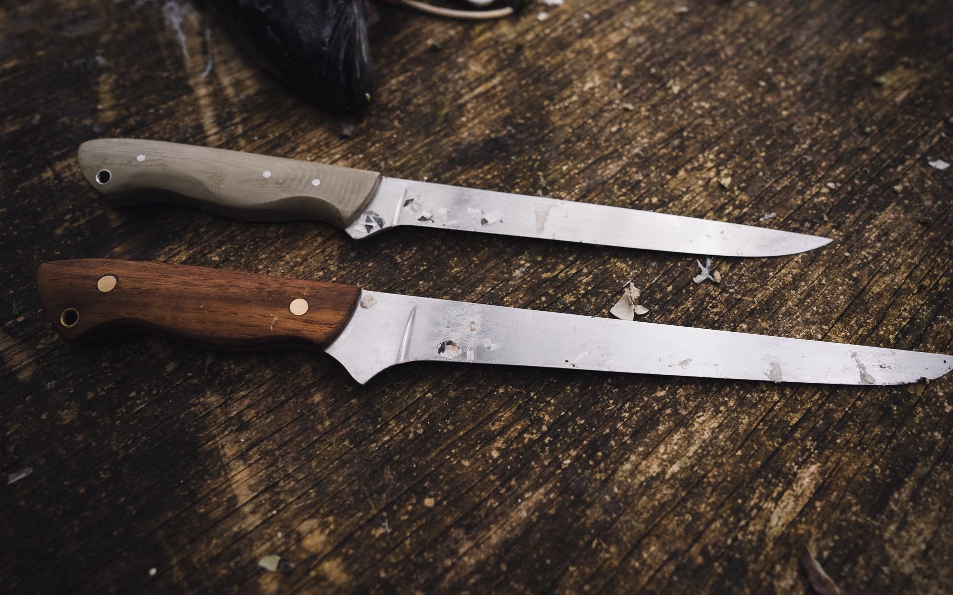 Two handmade filleting knives side by side, grey micarta handle above, timber handle below