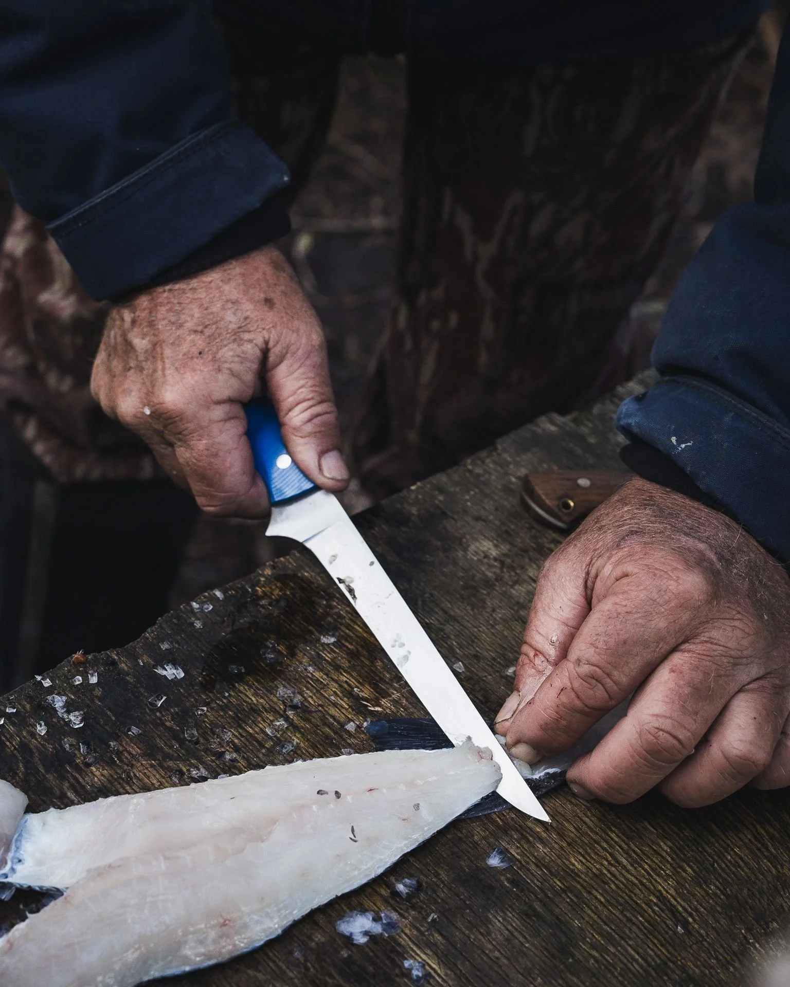 Filleting knife lifting a fillet, black Kydex sheath on the board beside it