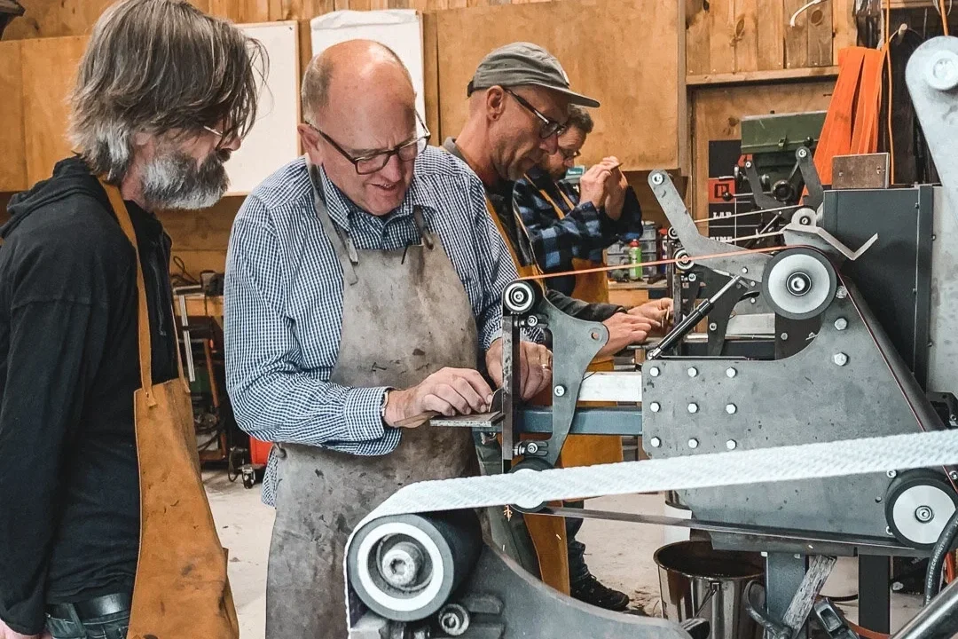 men in workshop using machines to grind carbon steel knife blades