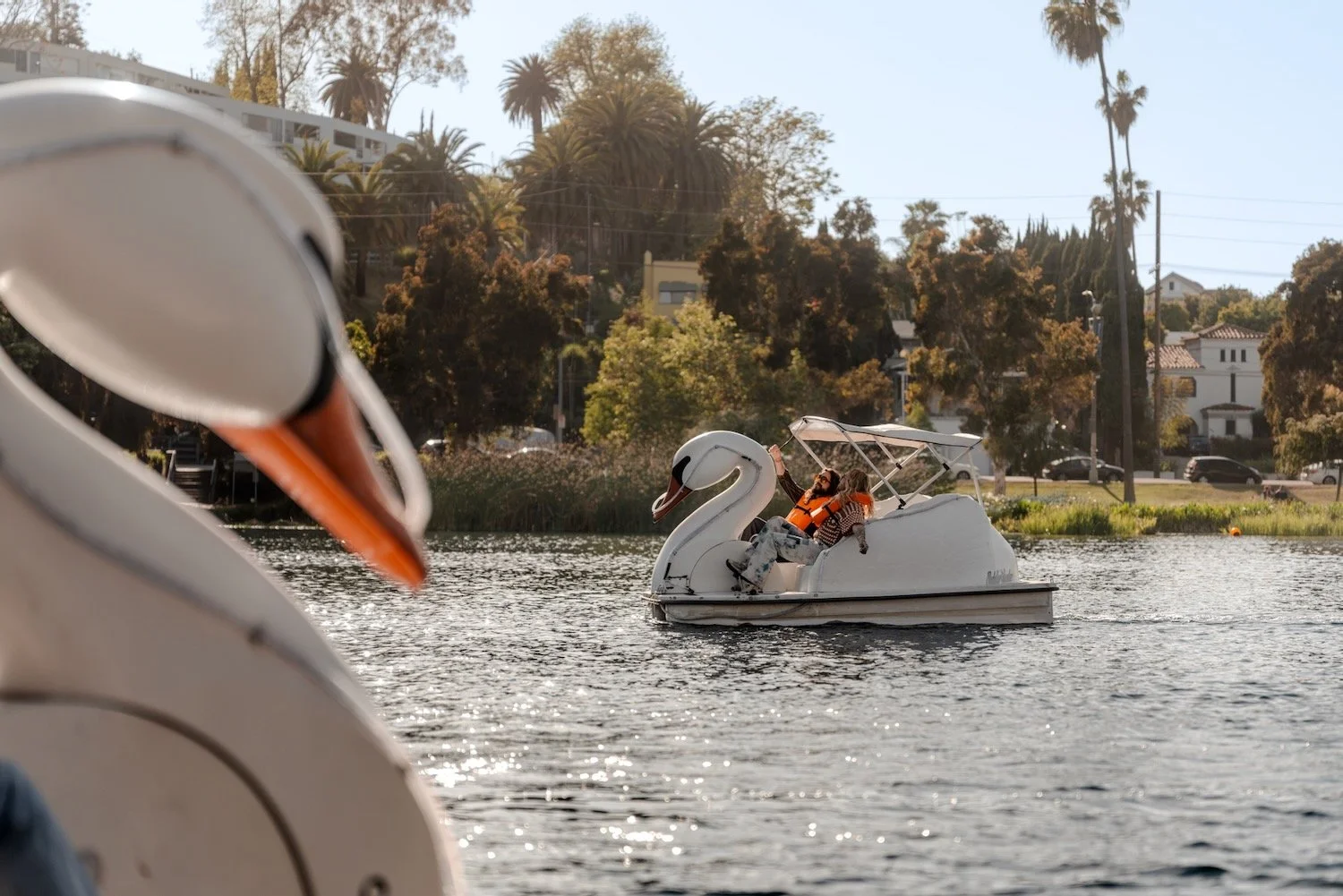 Bill and Tom Kaulitz pedal a swan boat on Echo Park Lake in Los Angeles, framed by a second swan boat in the foreground.