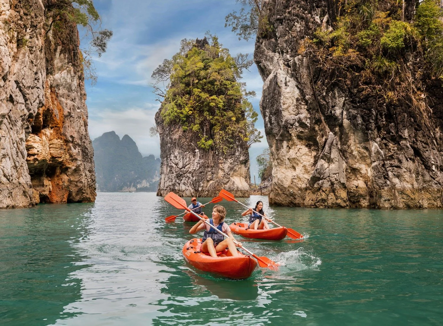 Traveler in a life vest on a lake boat, eyes closed, limestone cliffs behind, Khao Sok, Thailand. Make Memories campaign.