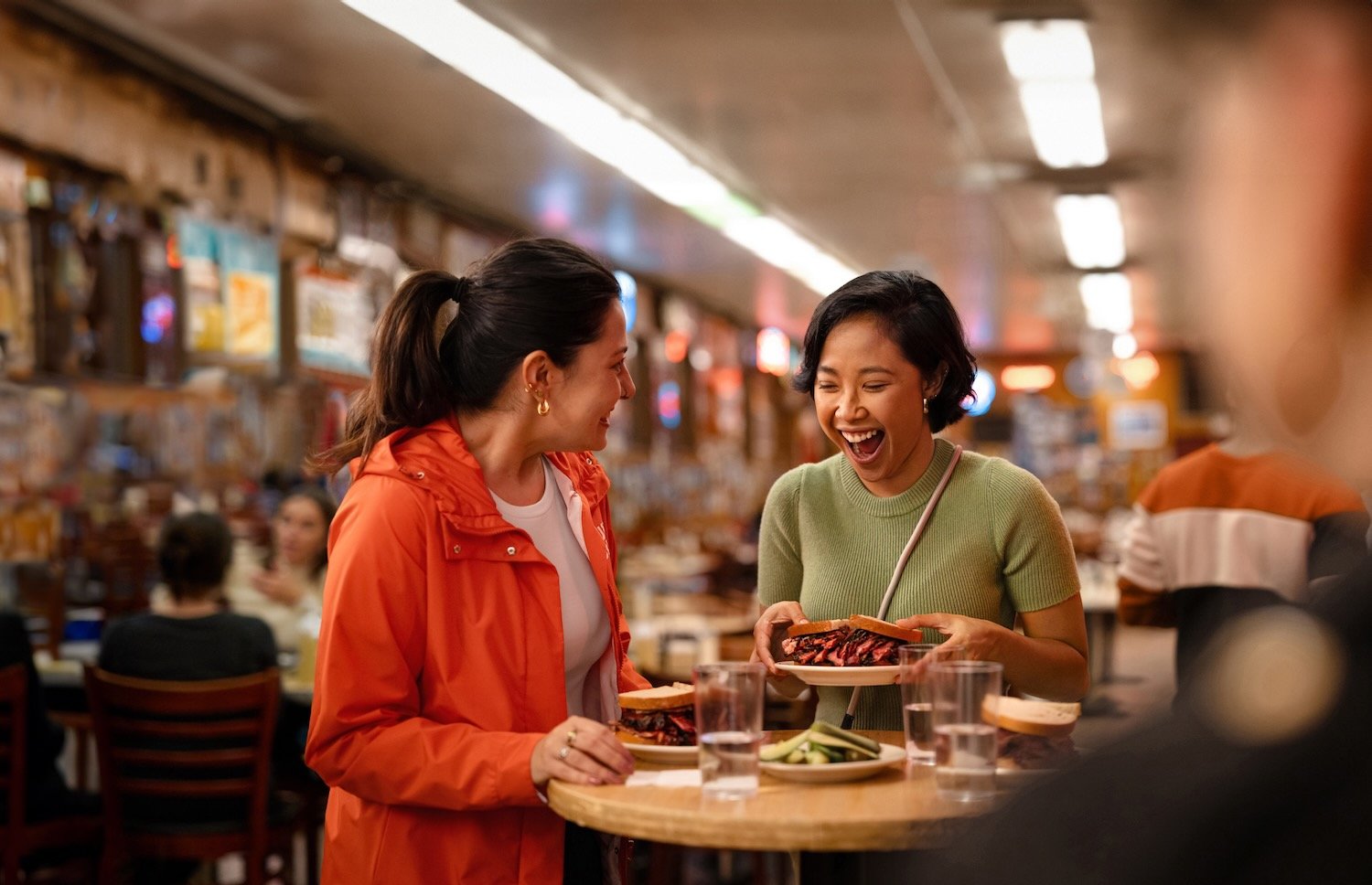 A traveler takes the first bite of the iconic sandwich at Katz’s Deli in New York, with the room behind.