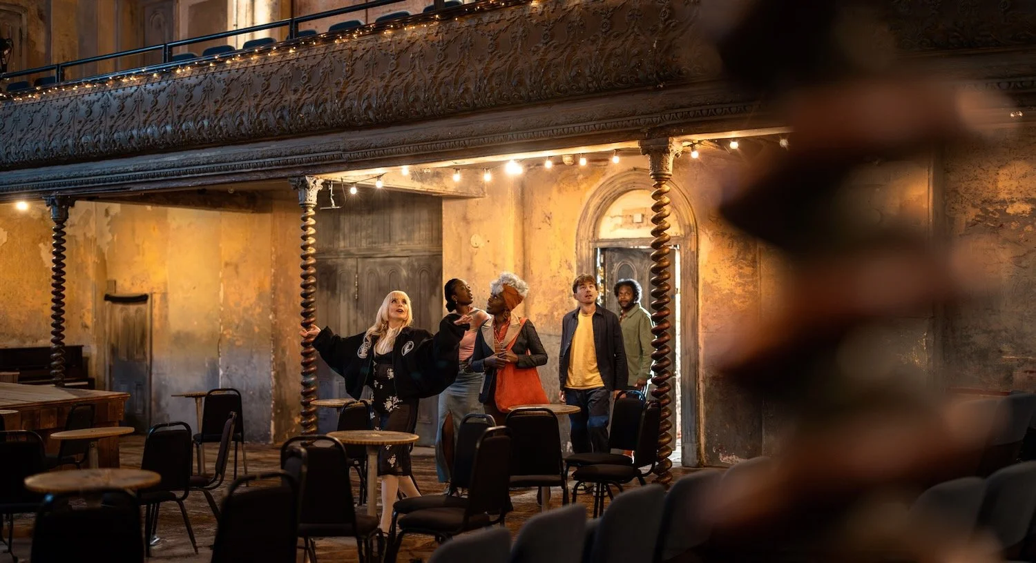 Paloma Faith points up at the balcony of Wilton's Music Hall as guests look on under strings of warm lights.