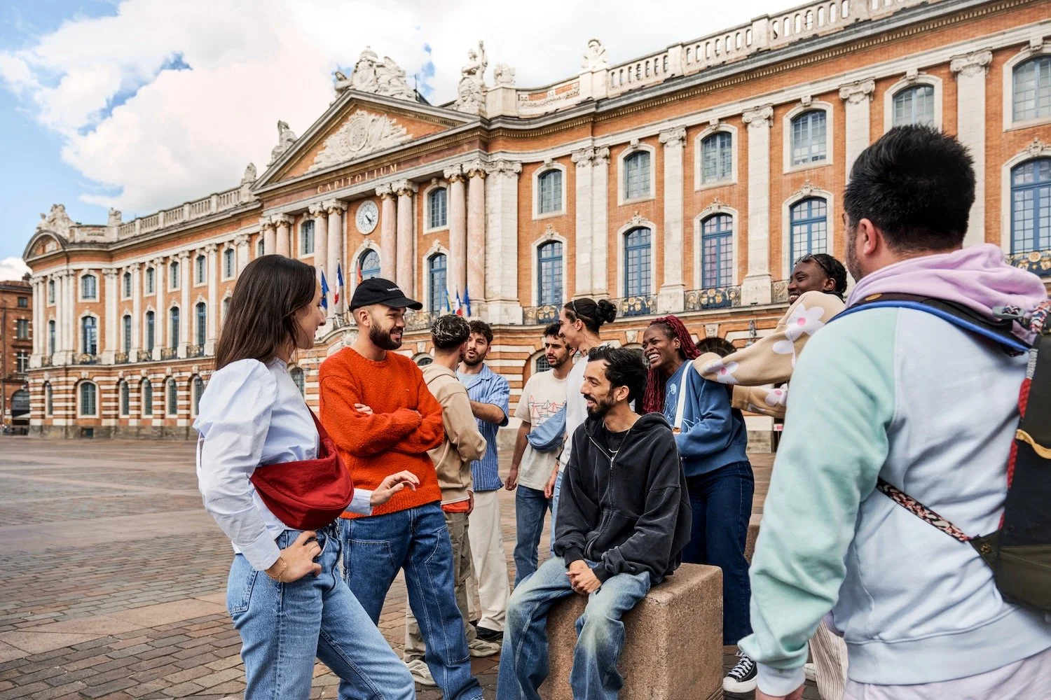 A group of travelers laughs with BigFlo & Oli on Place du Capitole in Toulouse.