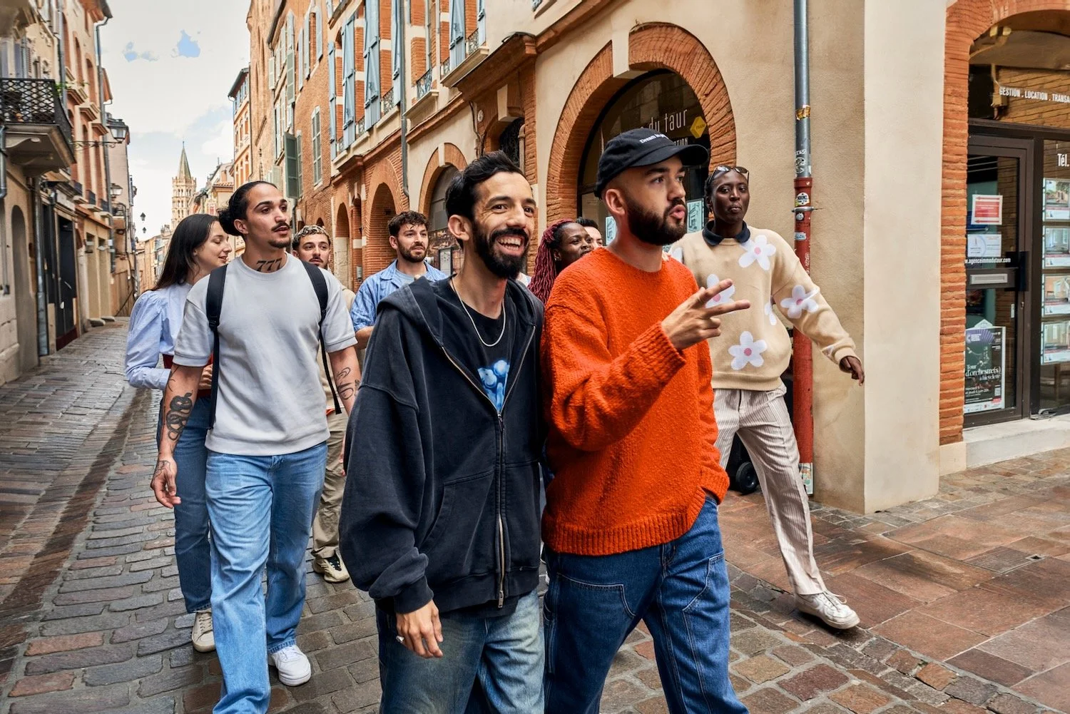 BigFlo & Oli lead a group of travelers down a narrow red-brick street in central Toulouse.