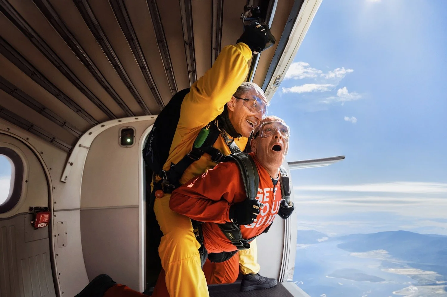 Tandem skydiver in a red jumpsuit mid-freefall, laughing, Empuriabrava, Spain. Make Memories campaign.