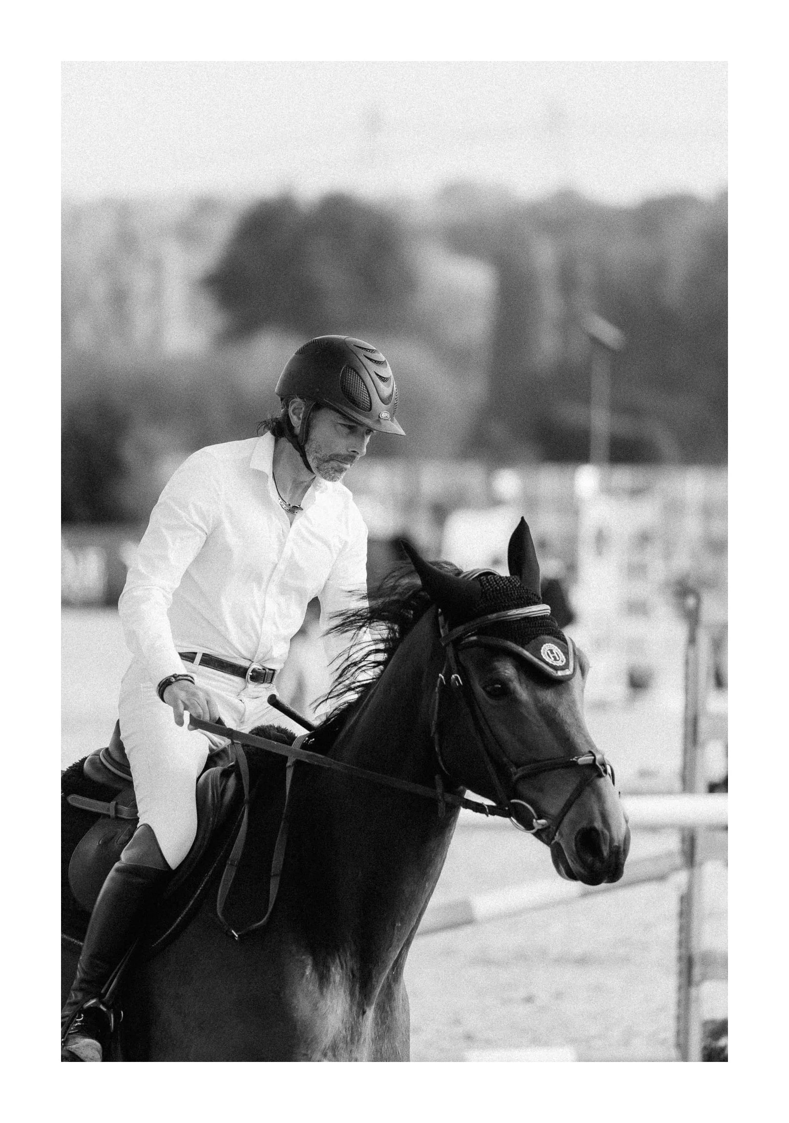 A man in a white shirt and riding helmet riding a horse on a racetrack.