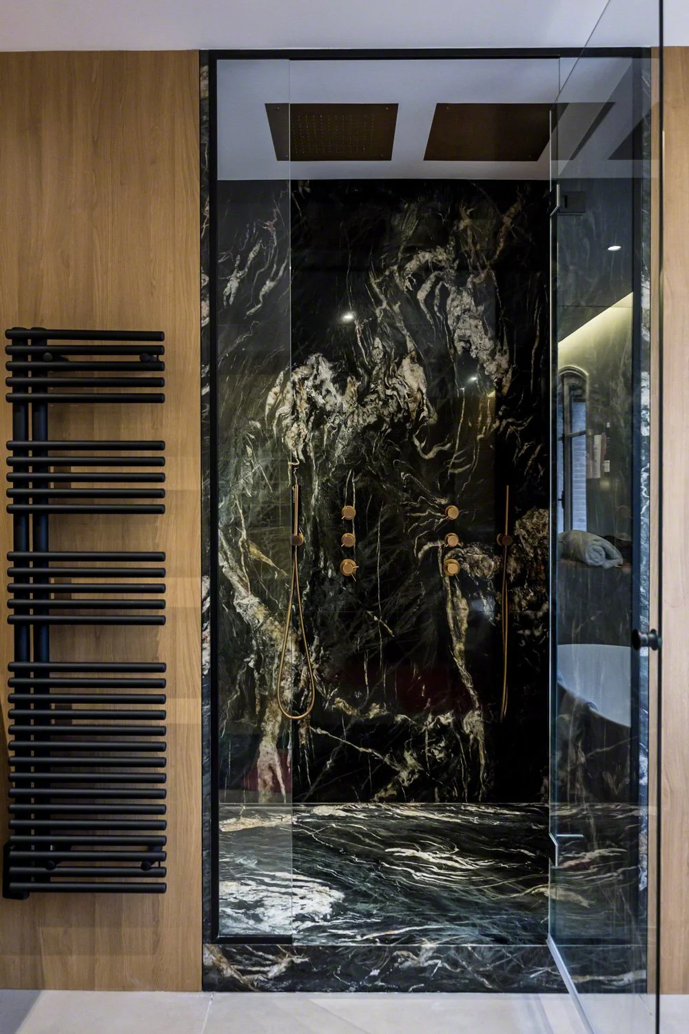 Modern shower with black marble walls and a glass door, adjacent to a wooden wall with black towel racks.
