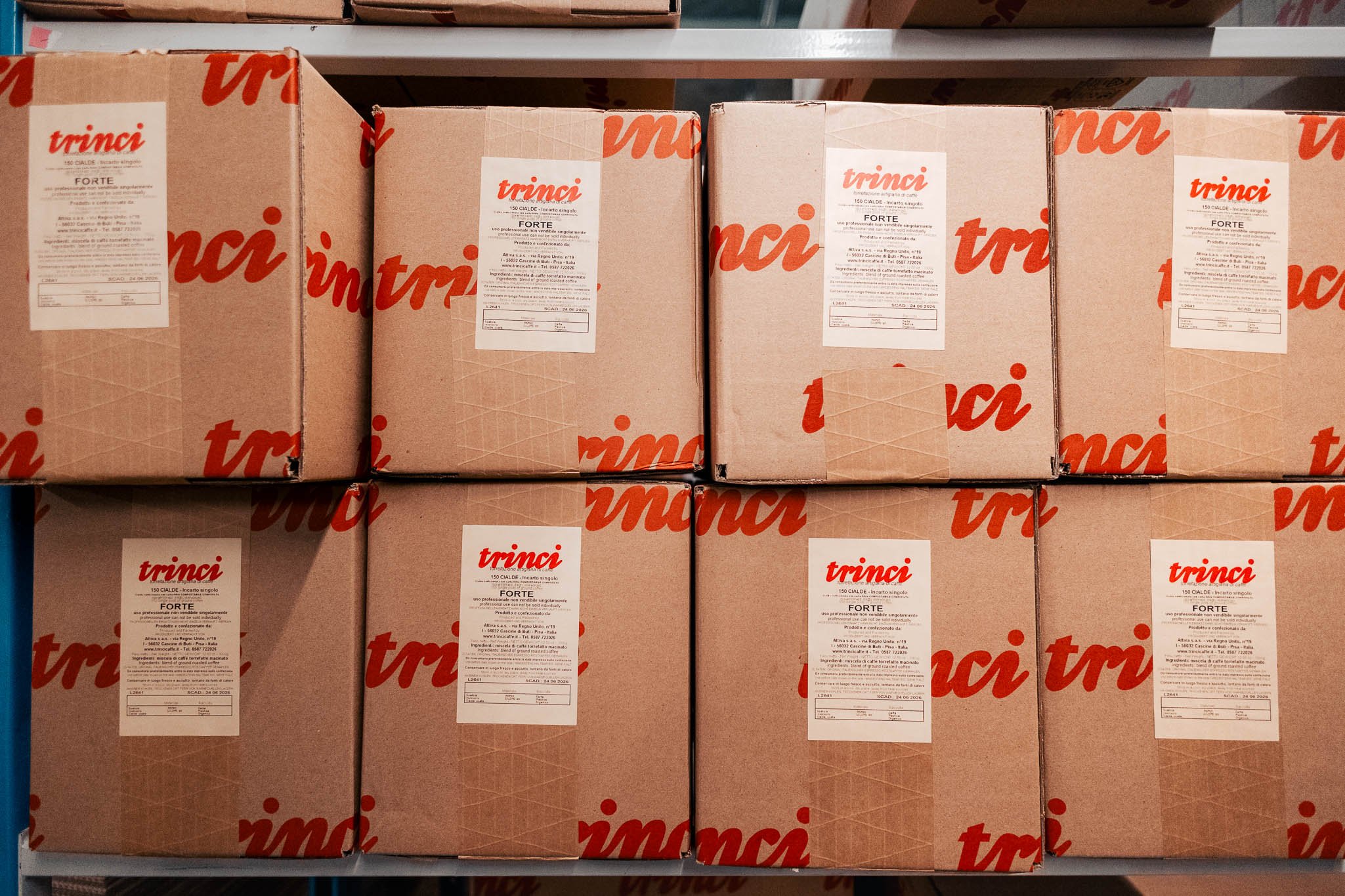 Stacks of cardboard boxes marked with the brand name 'Trinci' on a warehouse shelf.