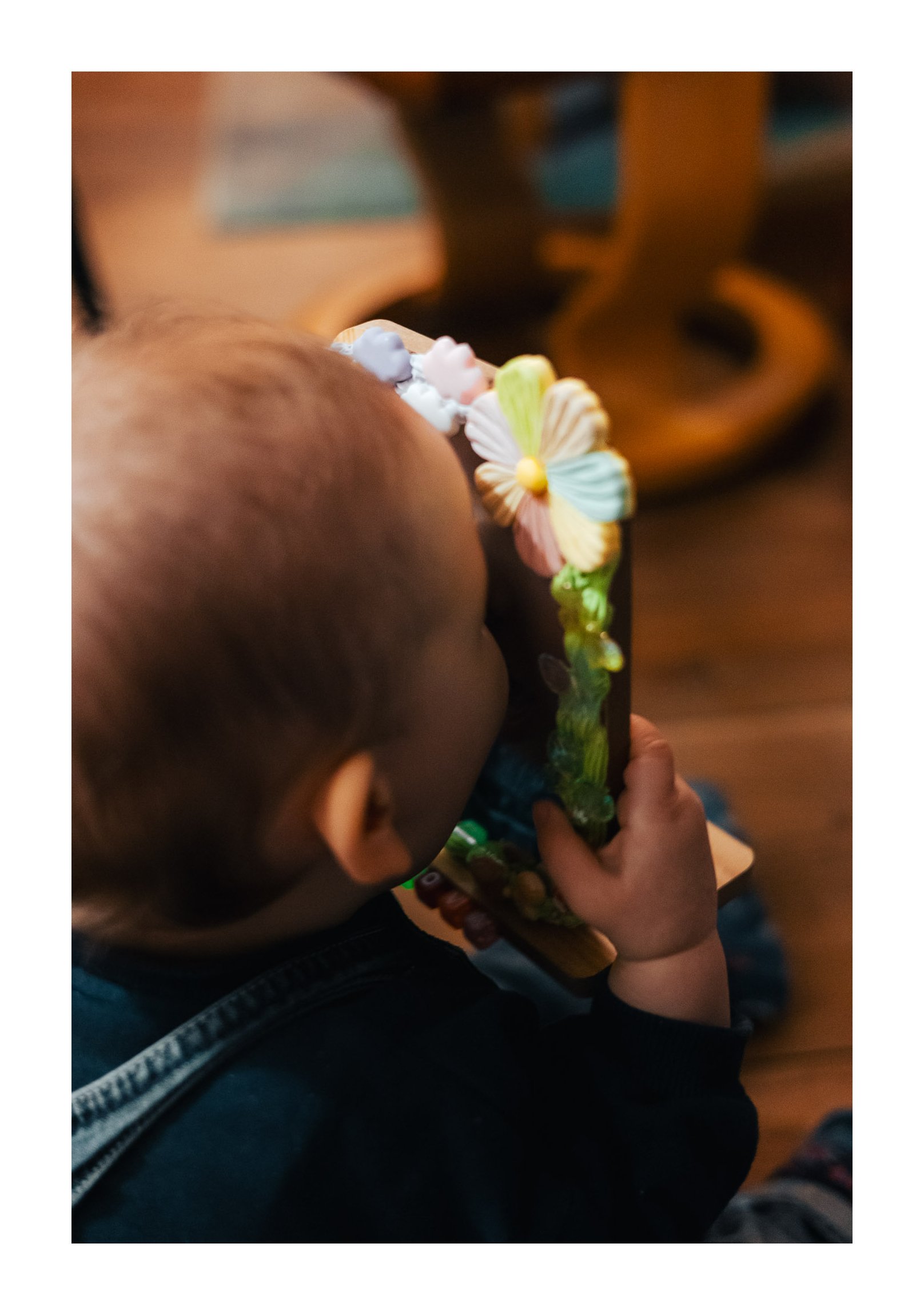 A young child in a dark shirt is holding and looking at a colorful birthday cake decorated with multicolored flowers and small figures, close to his face.