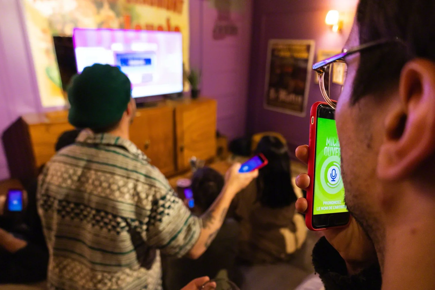 People watching television in a dimly lit room while recording or taking photos with their smartphones.
