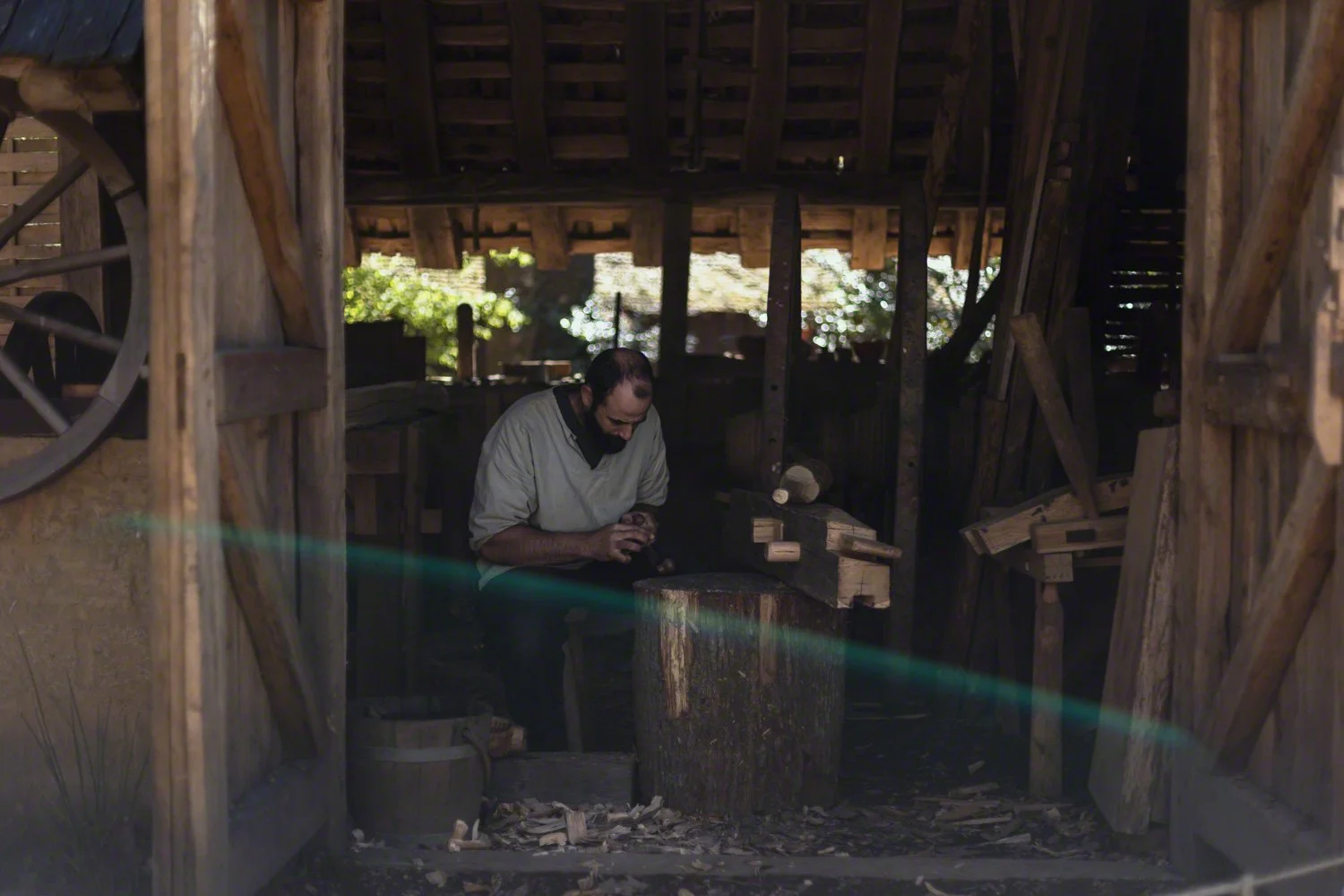 A man working on a wooden piece in a rustic workshop with wooden beams and tools.