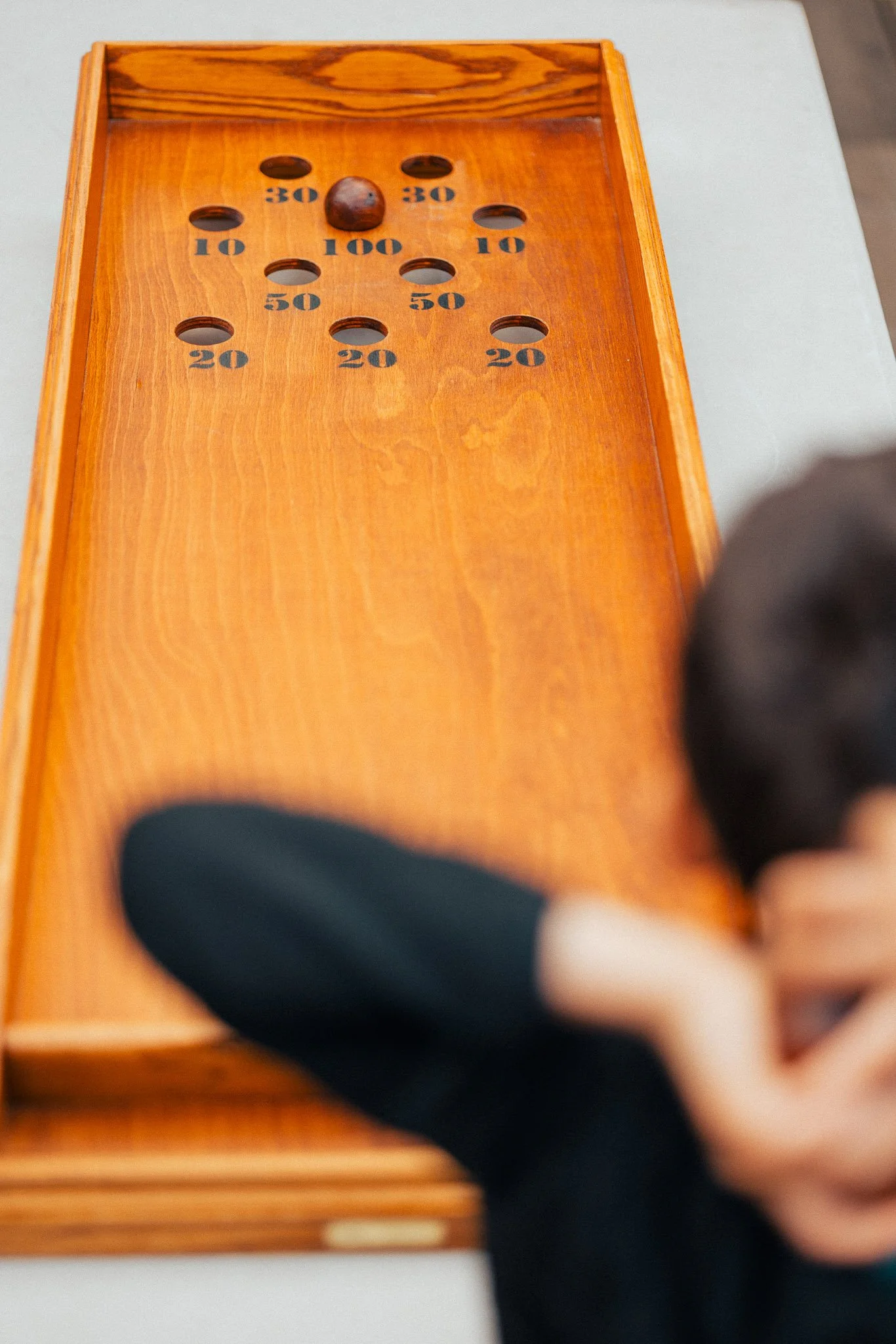 Close-up of a wooden shuffleboard game with numbered scoring zones and a puck, with a person's hand in the foreground.