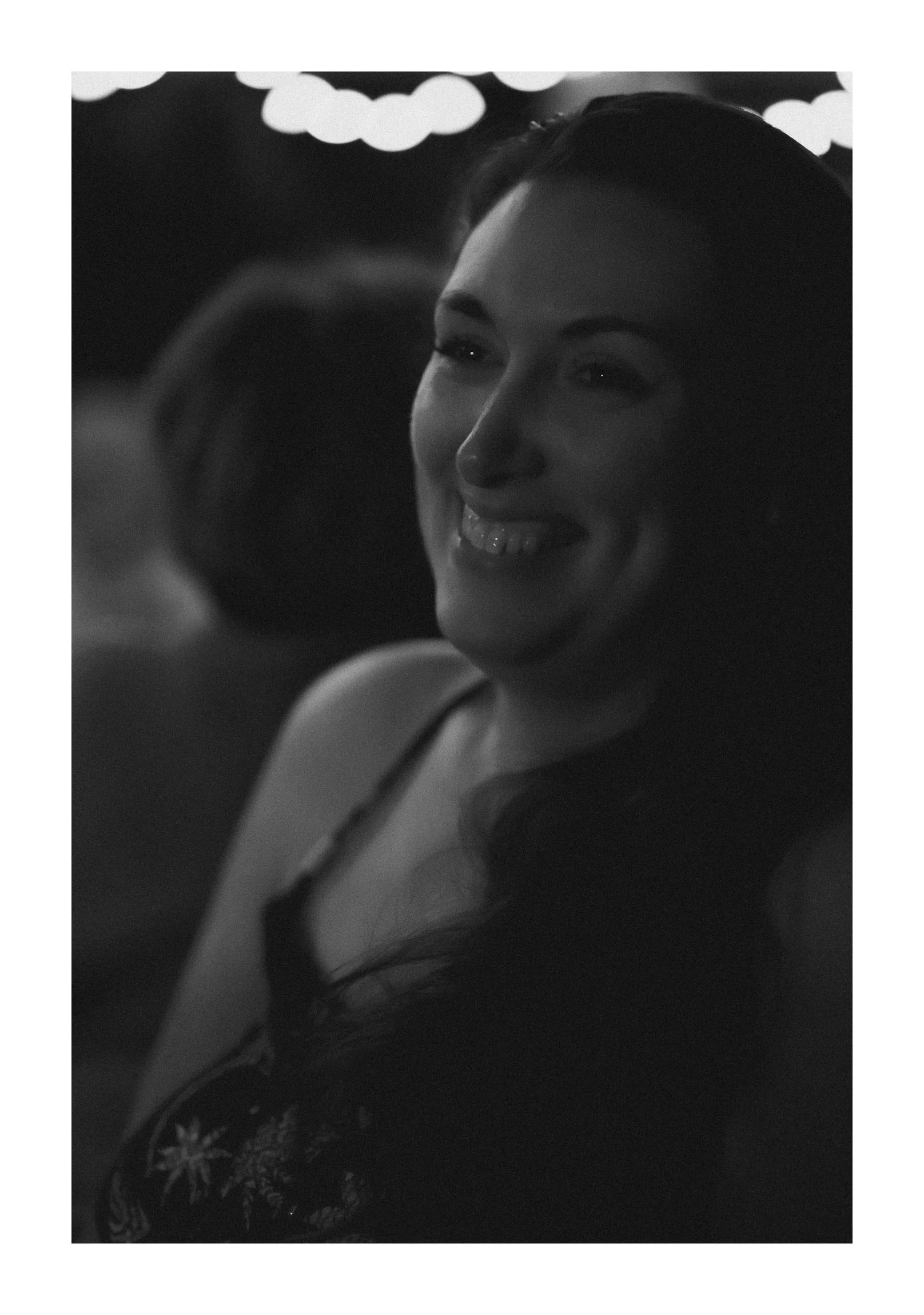 A woman with long dark hair smiling at an event, with decorative cloud-like shapes in the background.