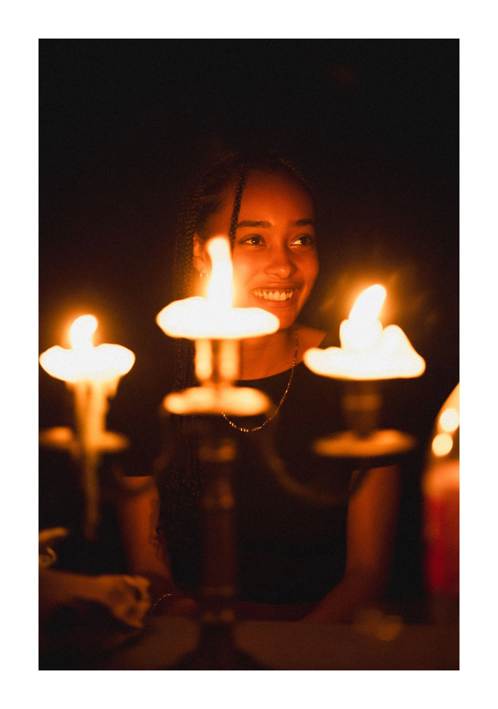 A young woman smiling at a birthday celebration surrounded by lit candles.