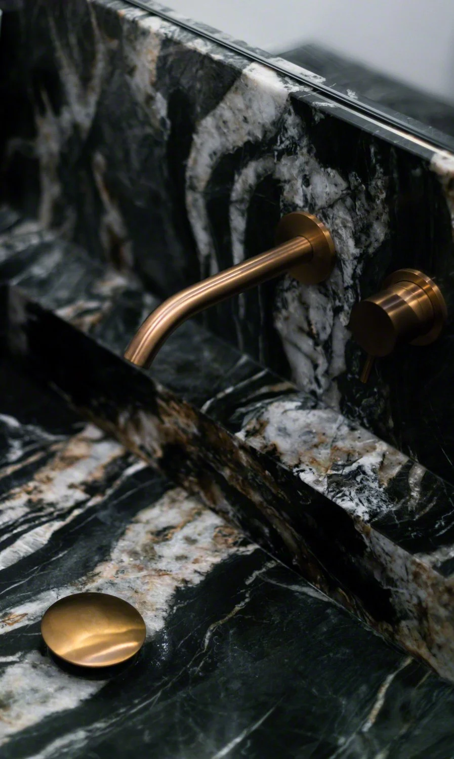 Close-up of a black and white marble sink with brass faucet and knobs.