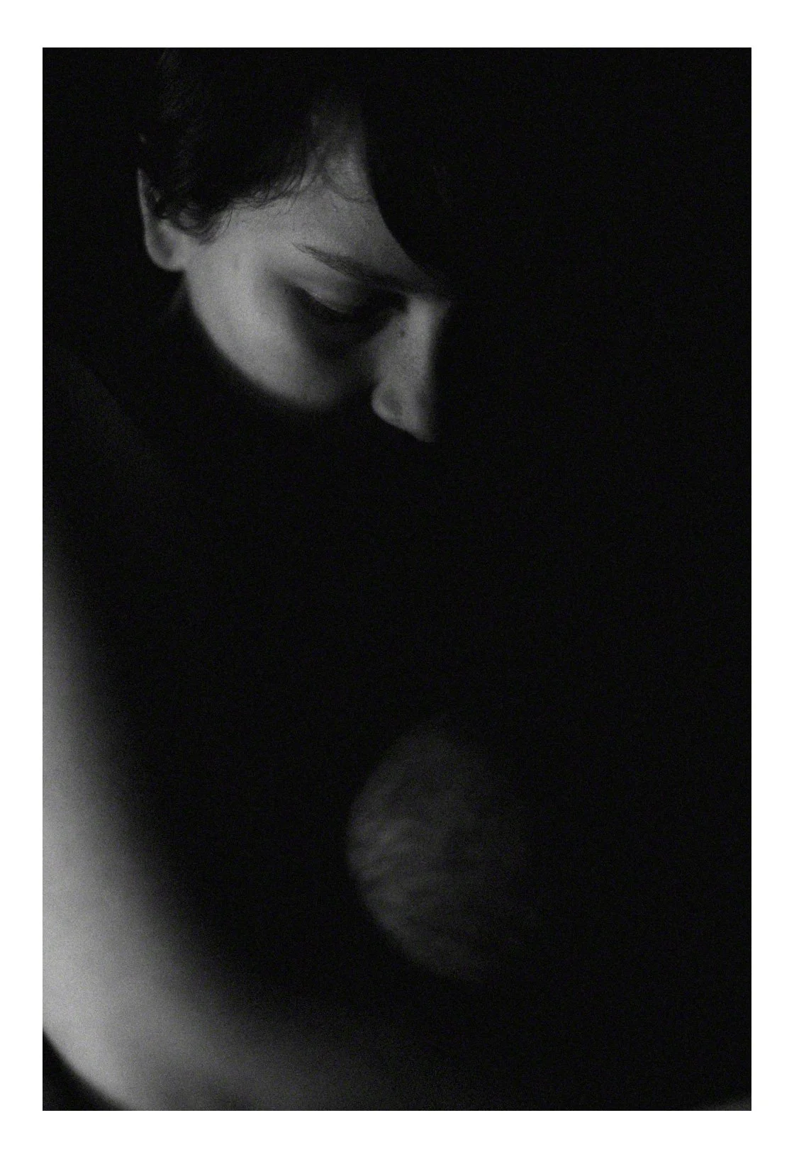 A grayscale photo of a person with short hair, eyes closed, and a serene expression, possibly resting or deep in thought.