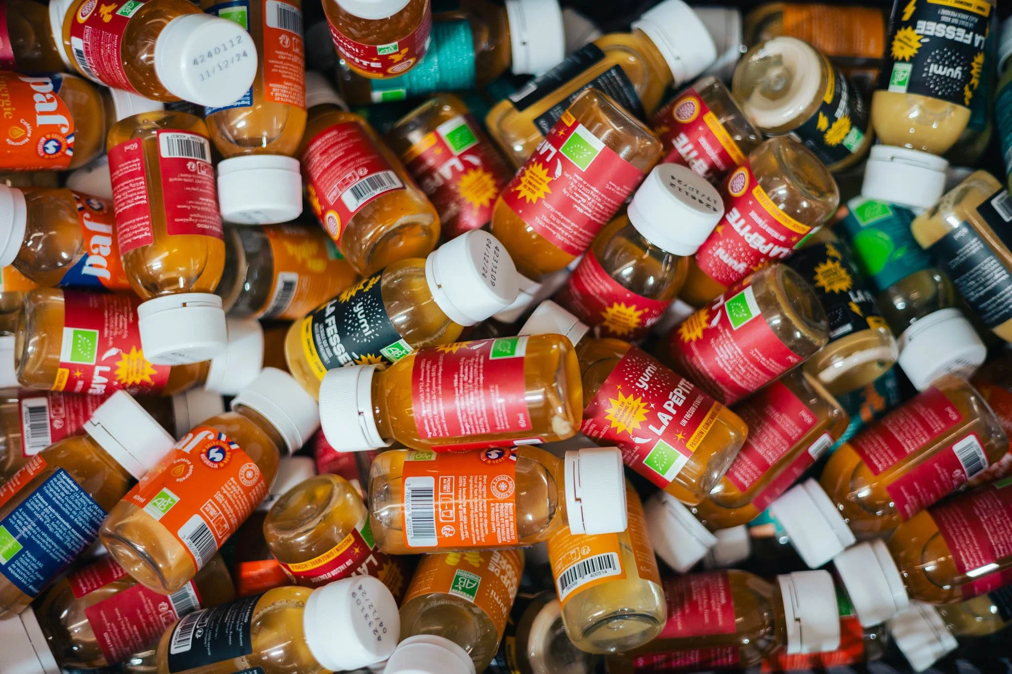 A collection of empty medicine bottles with white caps and red, green, blue, and black labels, piled together.