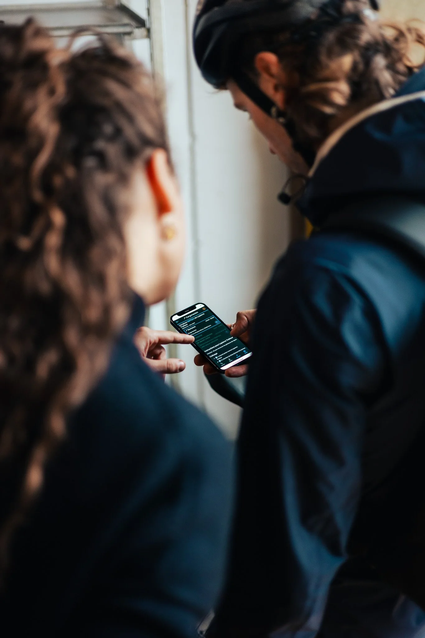Two people standing close together, looking at a smartphone held by one of them with a dark-themed screen displaying text.
