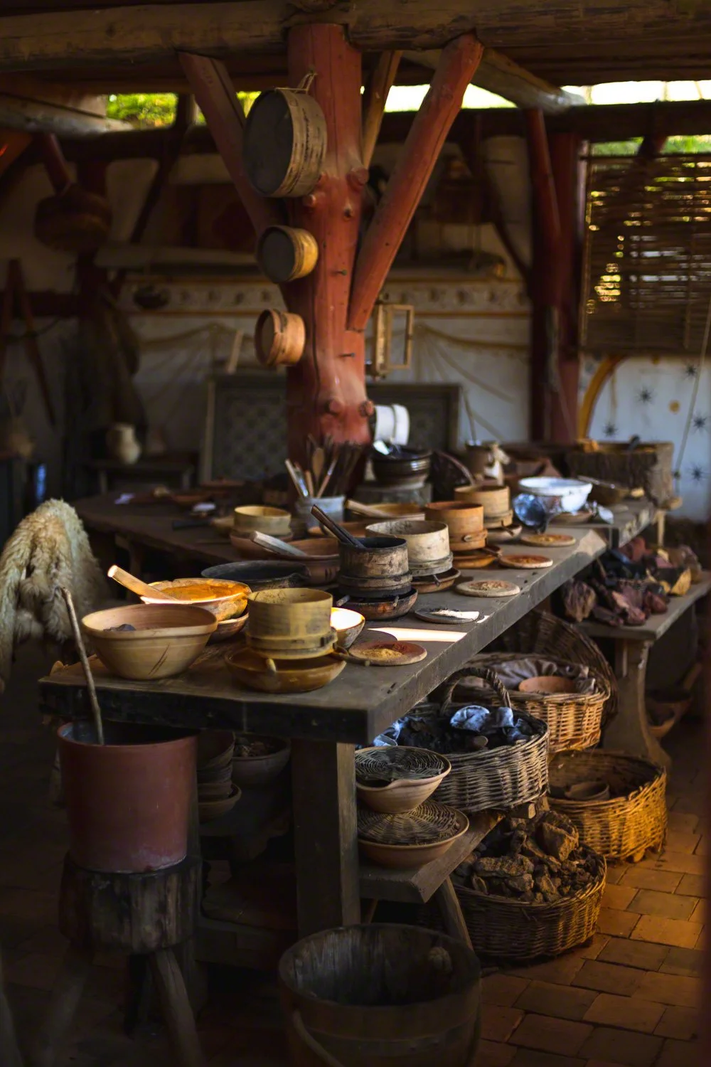 A rustic display of handmade pottery and wooden bowls on a long wooden table inside a cozy, wooden-walled shop with baskets of rocks and other decorative items.
