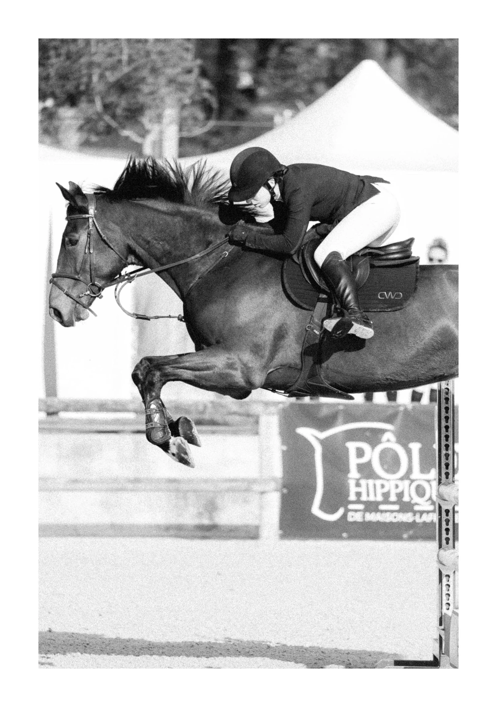 A female equestrian rider in riding gear and helmet, jumping a horse over an obstacle during a show jumping competition.