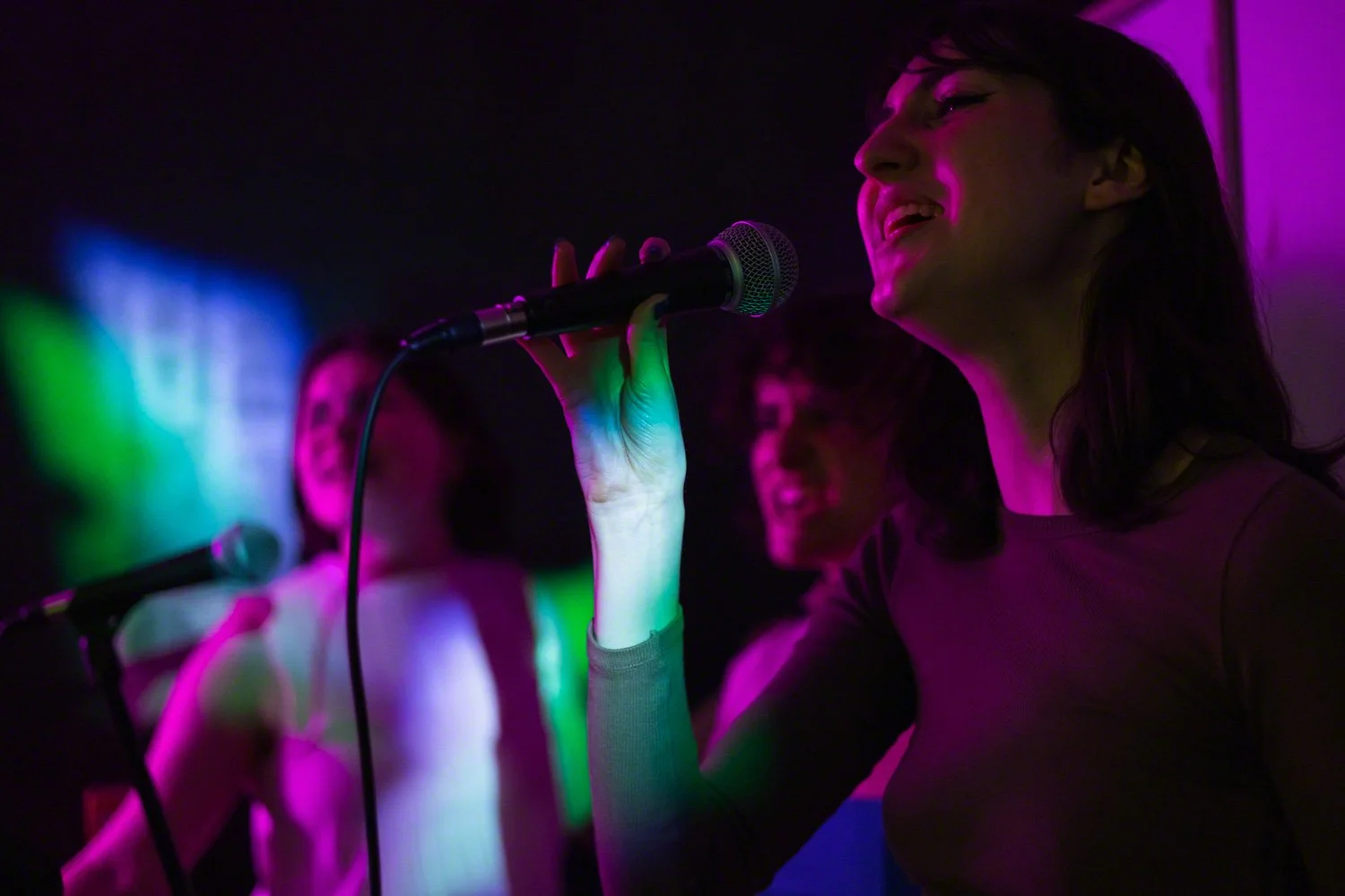 Group of women singing karaoke in a dimly lit room with colorful neon lights.