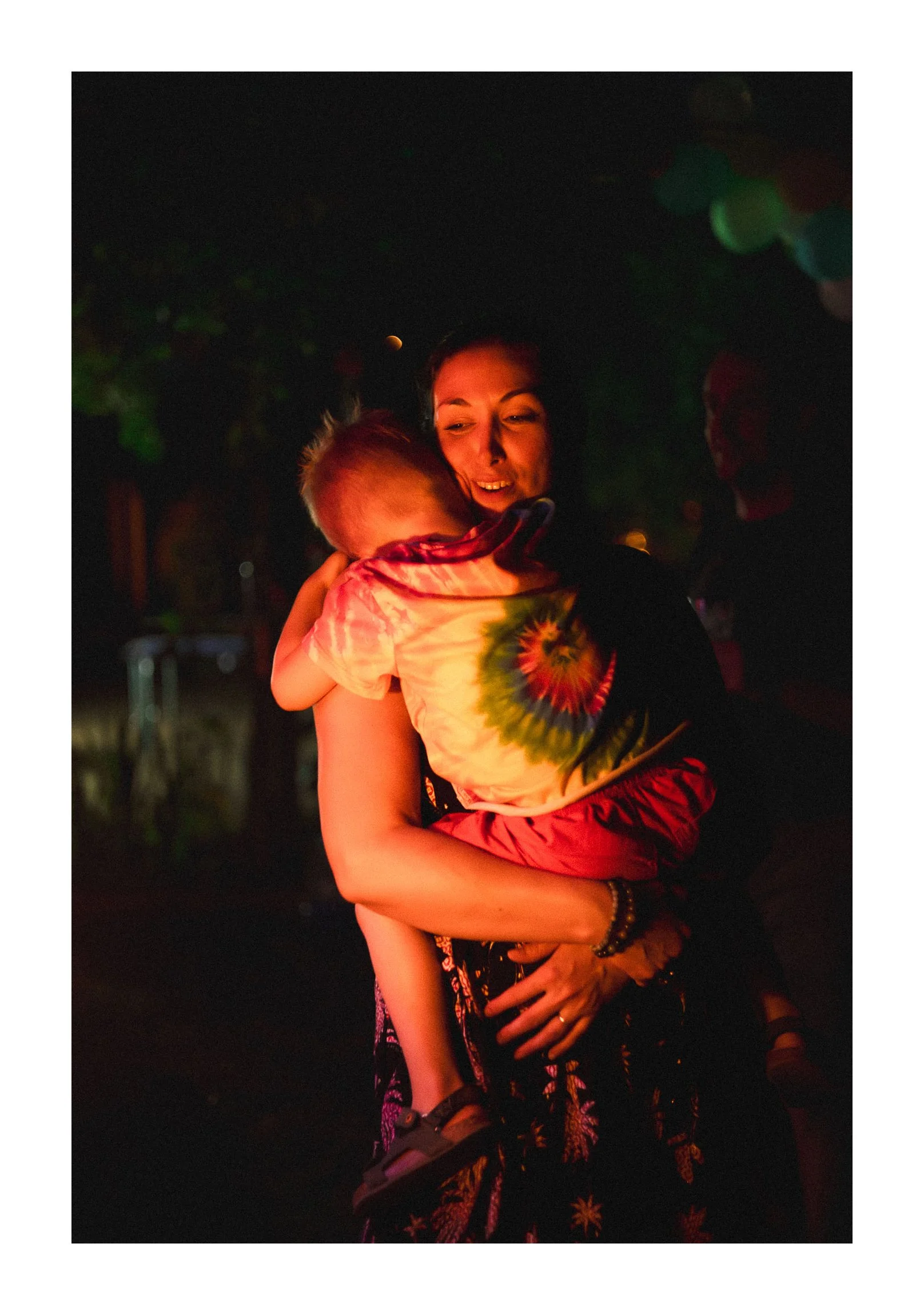 A woman happily hugging a young child at night, with trees and a moon in the background.