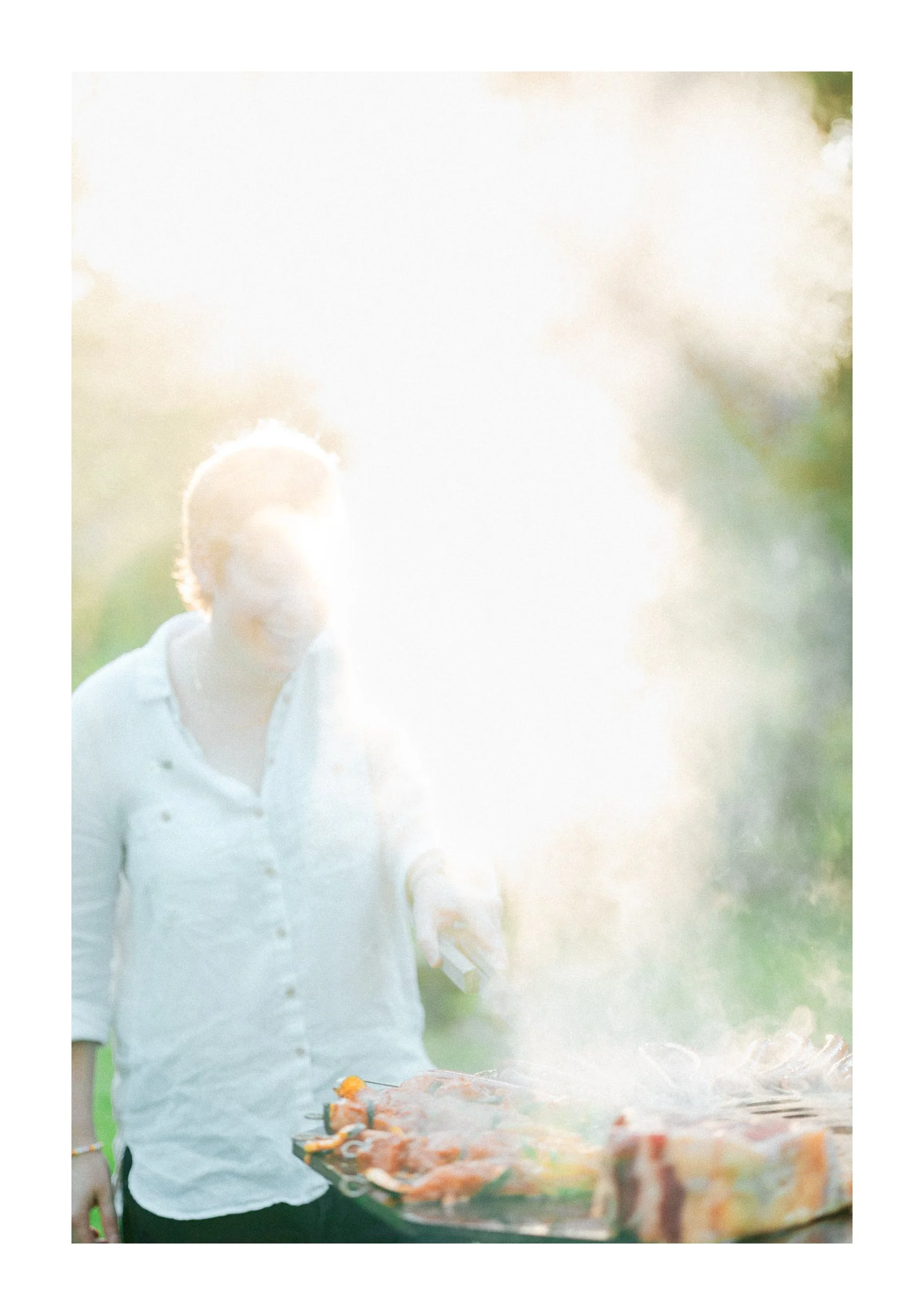 Person grilling barbecue outdoors with smoke rising from the grill.