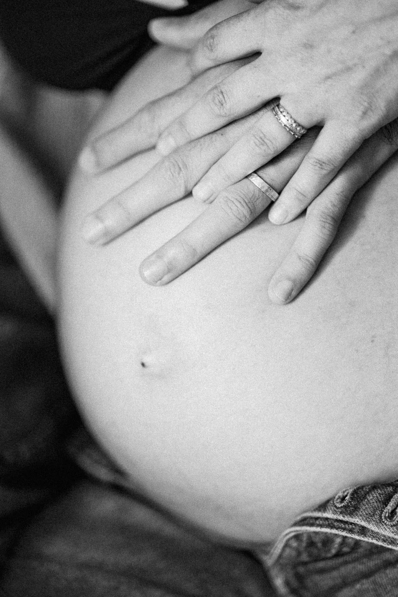 Black and white photo of a pregnant woman with hands on her belly, wearing wedding rings.