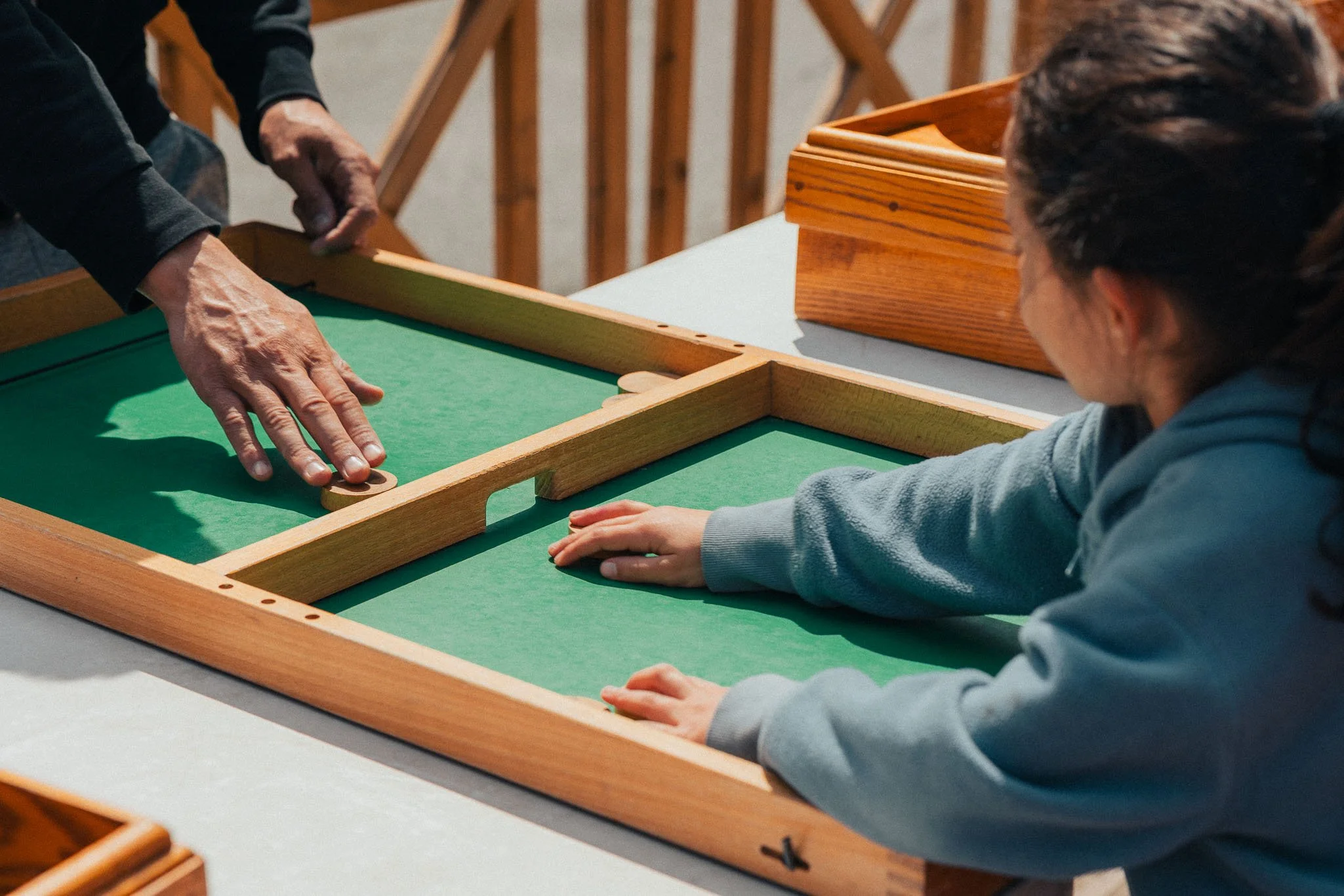 Two people playing a game of carrom on a wooden table with green surface, one person is using a striker while the other is observing.