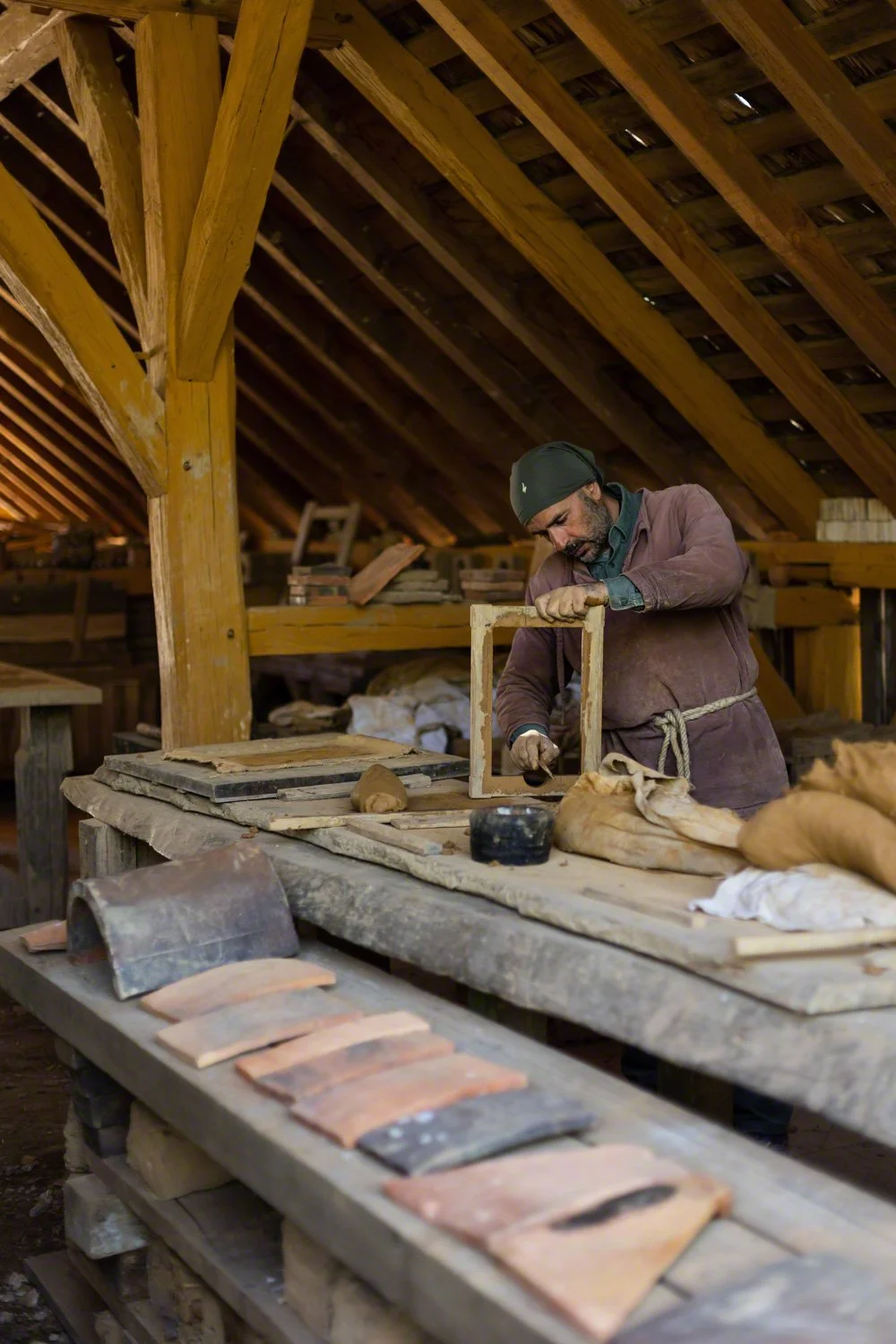 A man working on a woodworking project inside a rustic wooden workshop, surrounded by workbenches and tools.
