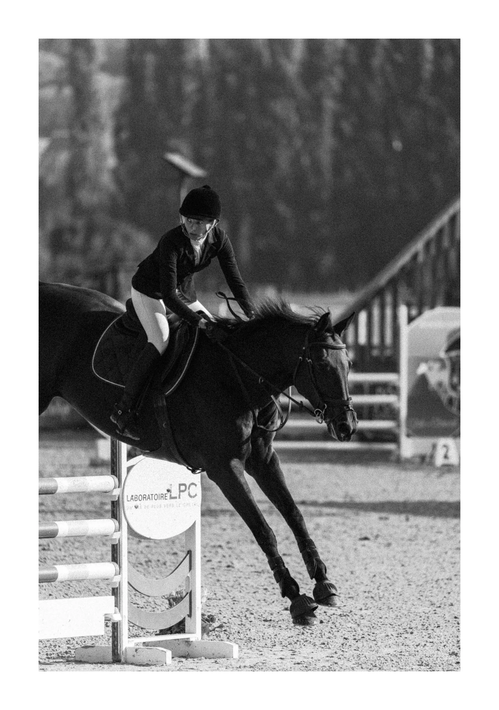 A person riding a horse in an equestrian event, jumping over an obstacle on an outdoor arena, in black and white.