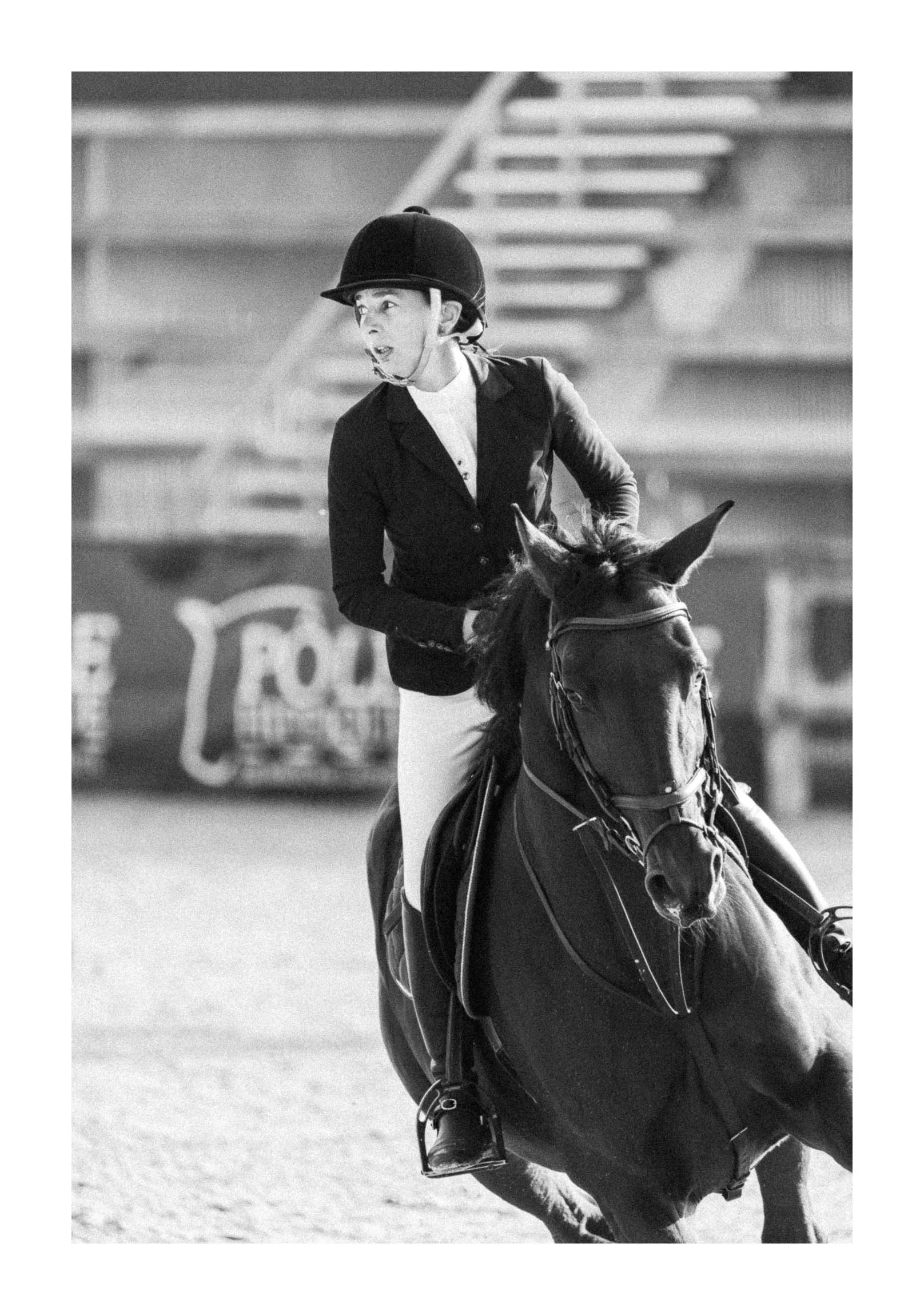 A woman wearing a riding helmet and equestrian attire riding a horse in a competitive event.