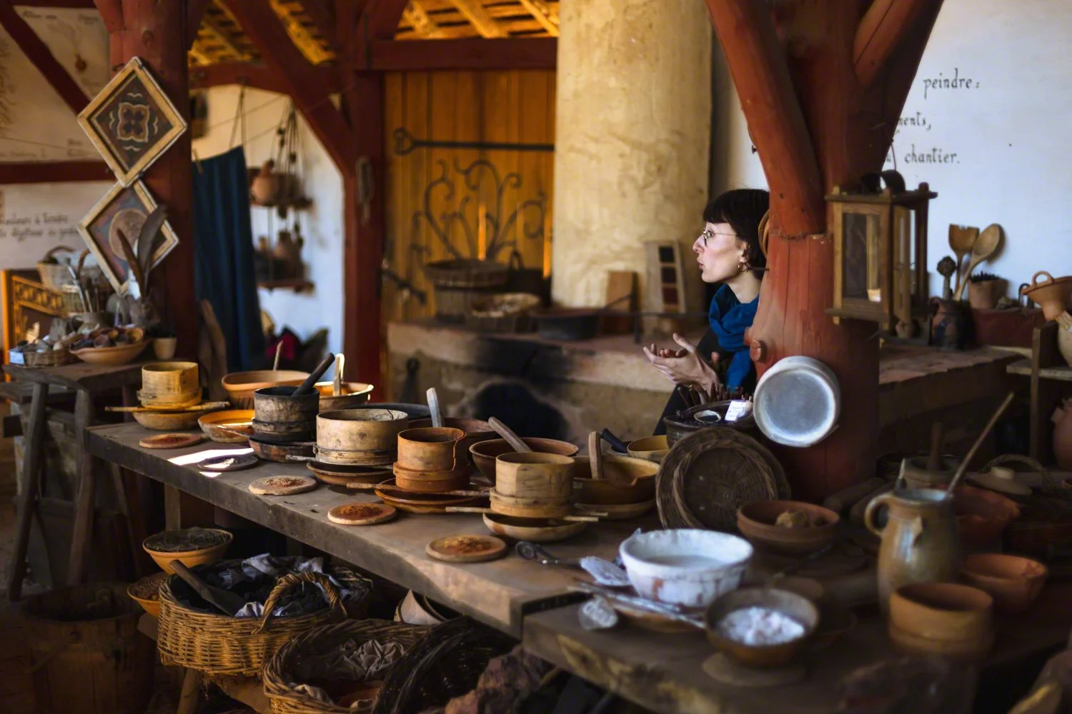 A woman inside a rustic shop with wooden beams, surrounded by handmade pottery and kitchenware on display.
