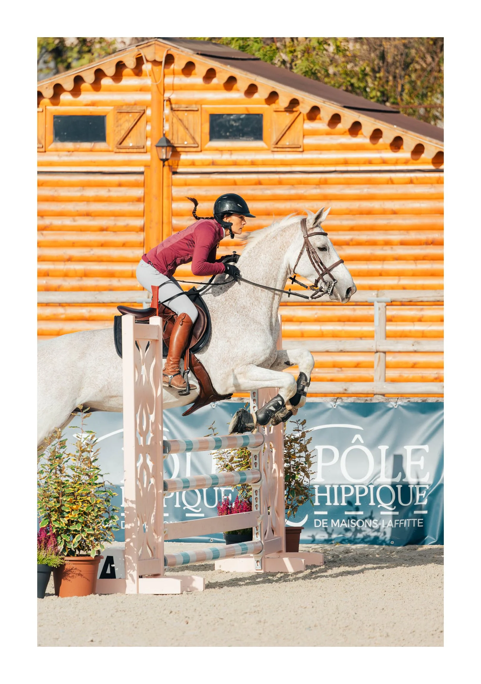 A woman riding a white horse jumps over a show jumping obstacle during an equestrian event.