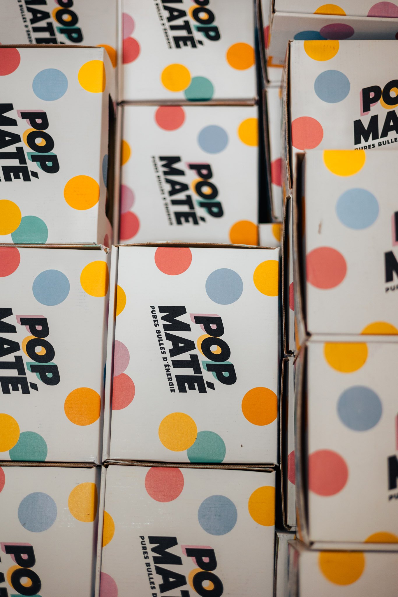 Close-up of boxes for Pop'Maté, an energy product, stacked on a shelf with colorful polka dot designs.