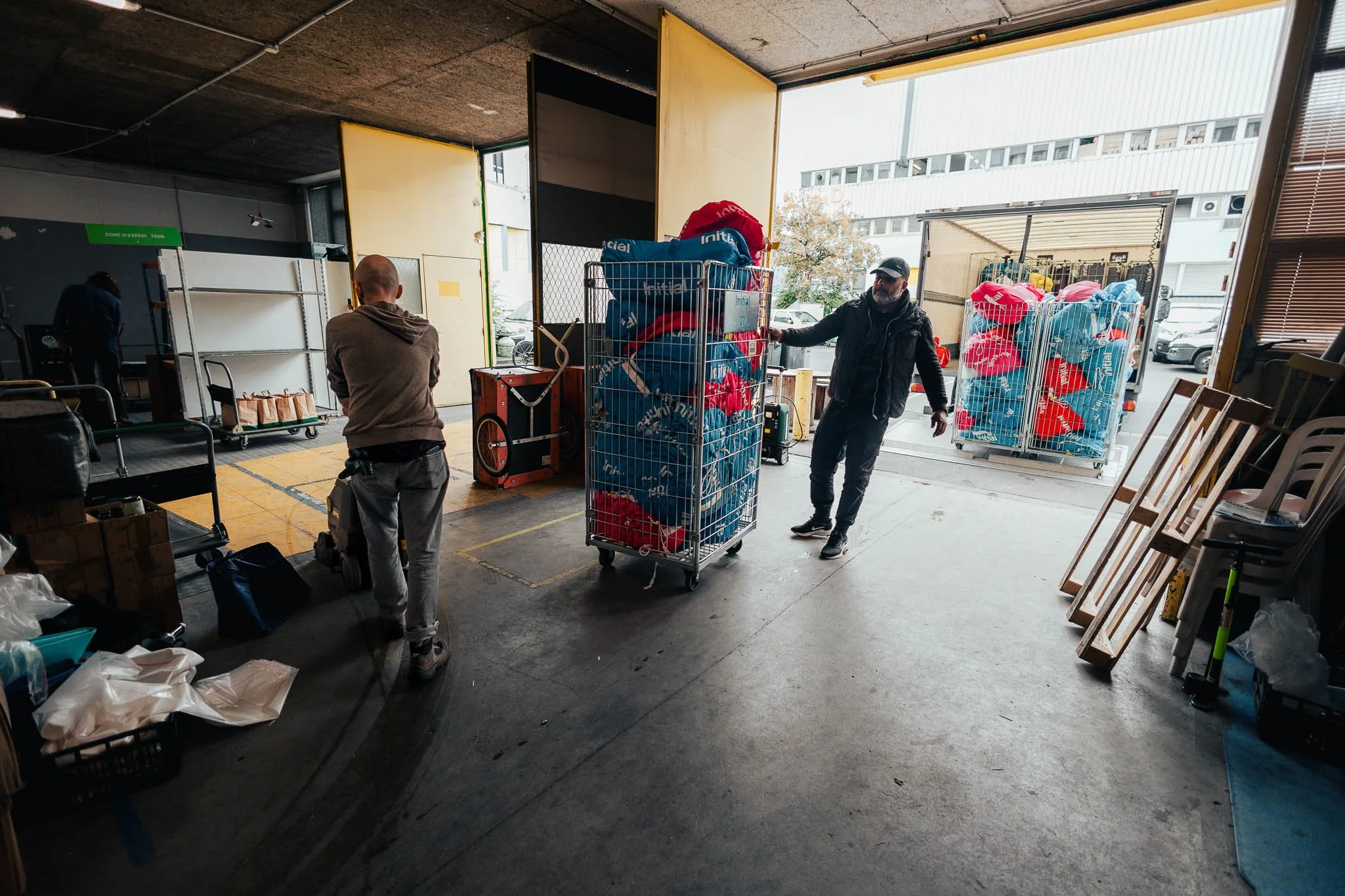 People unloading large carts filled with plastic bags outside a warehouse or loading dock.