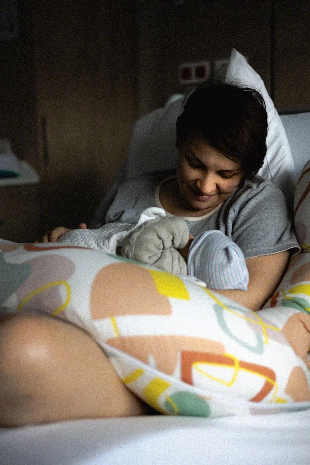 A woman smiles while holding a newborn baby in a hospital bed.
