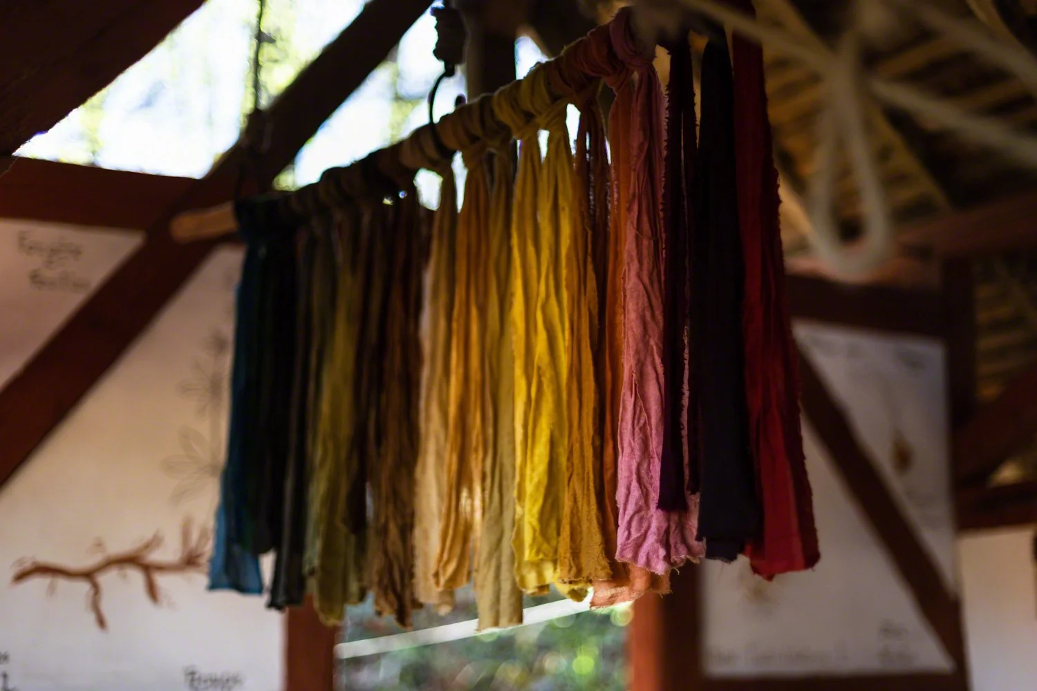 Colorful fabric strips hanging on a wooden rod with outdoor natural light in the background.