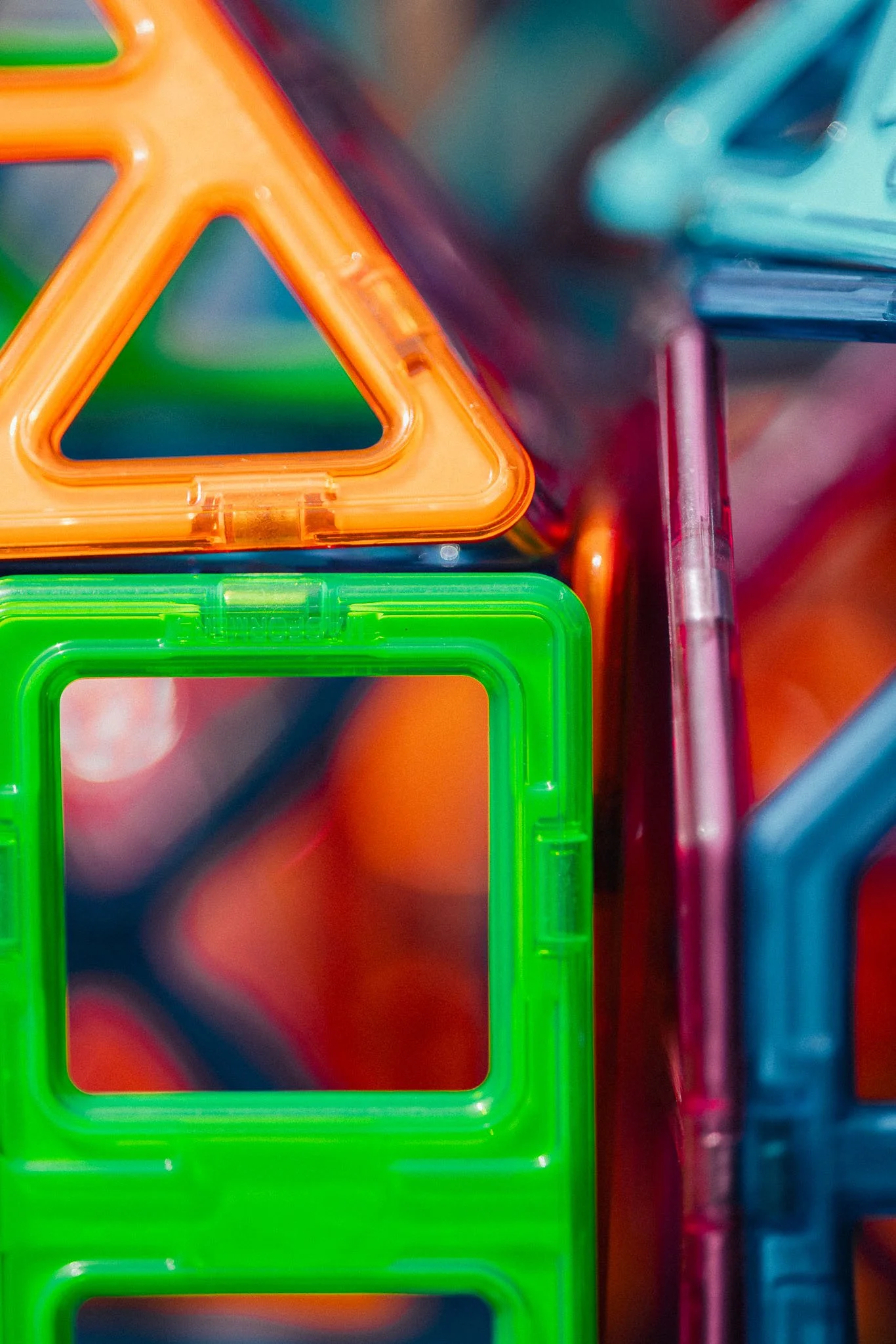 Close-up of colorful plastic geometric construction blocks, including a green square and an orange triangle.